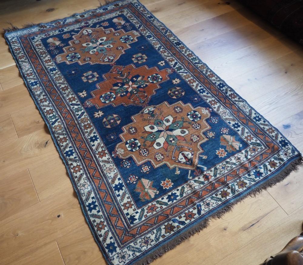 Ancien tapis caucasien Derbent à triple médaillon
Circa 1900

Le tapis comporte trois médaillons d'une douce couleur orange / marron délavée, qui ressortent bien sur le champ bleu indigo. Le tapis est encadré par deux bordures étoilées sur fond