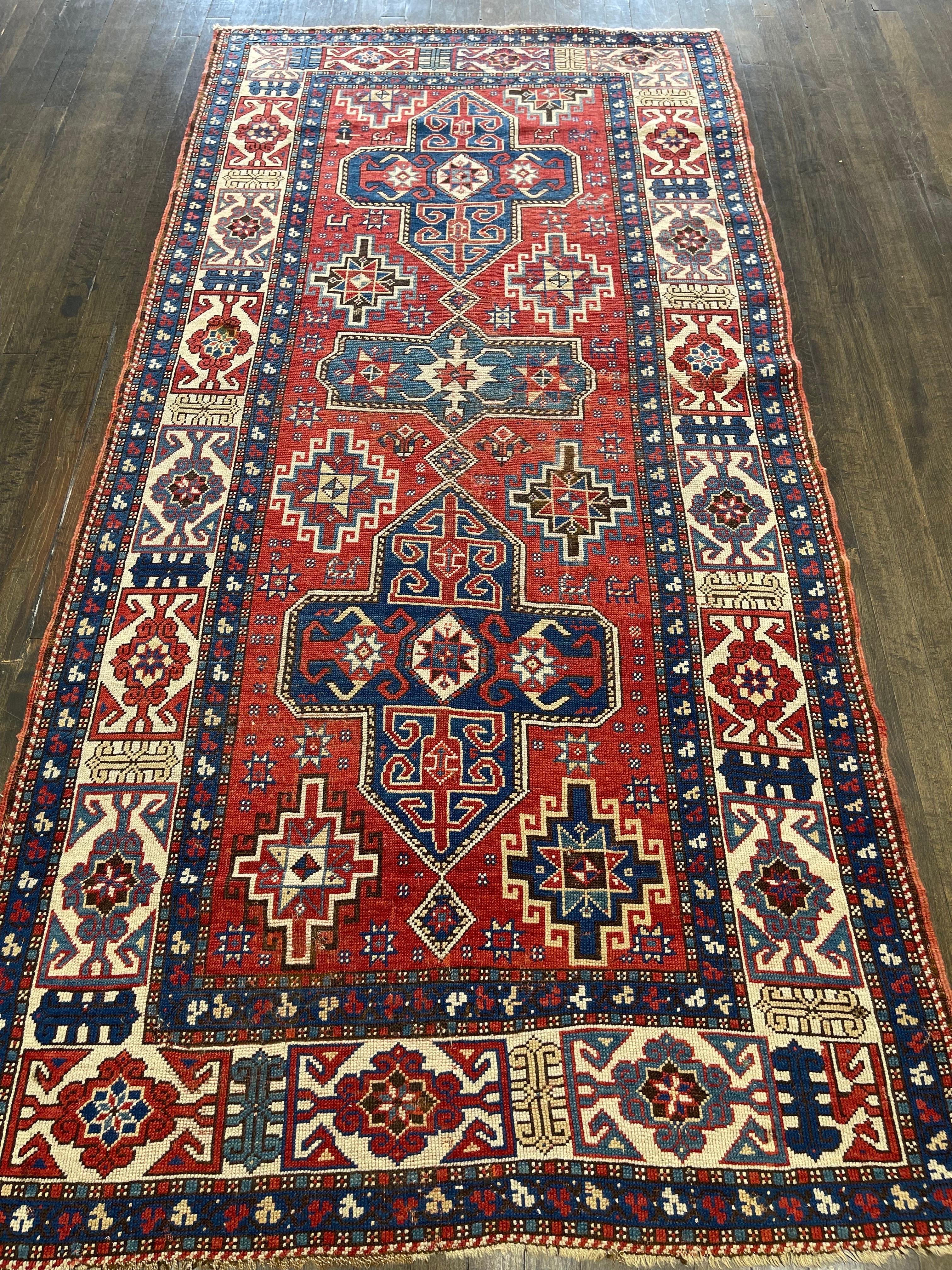 A stunning example of a caucasian Fachralo Kazak, featuring a clear crispy red field decorated with two medallions of medium blue colors and one smaller medallion in green. Ornaments throughout this Kazak are known as Memling guls,to be precise