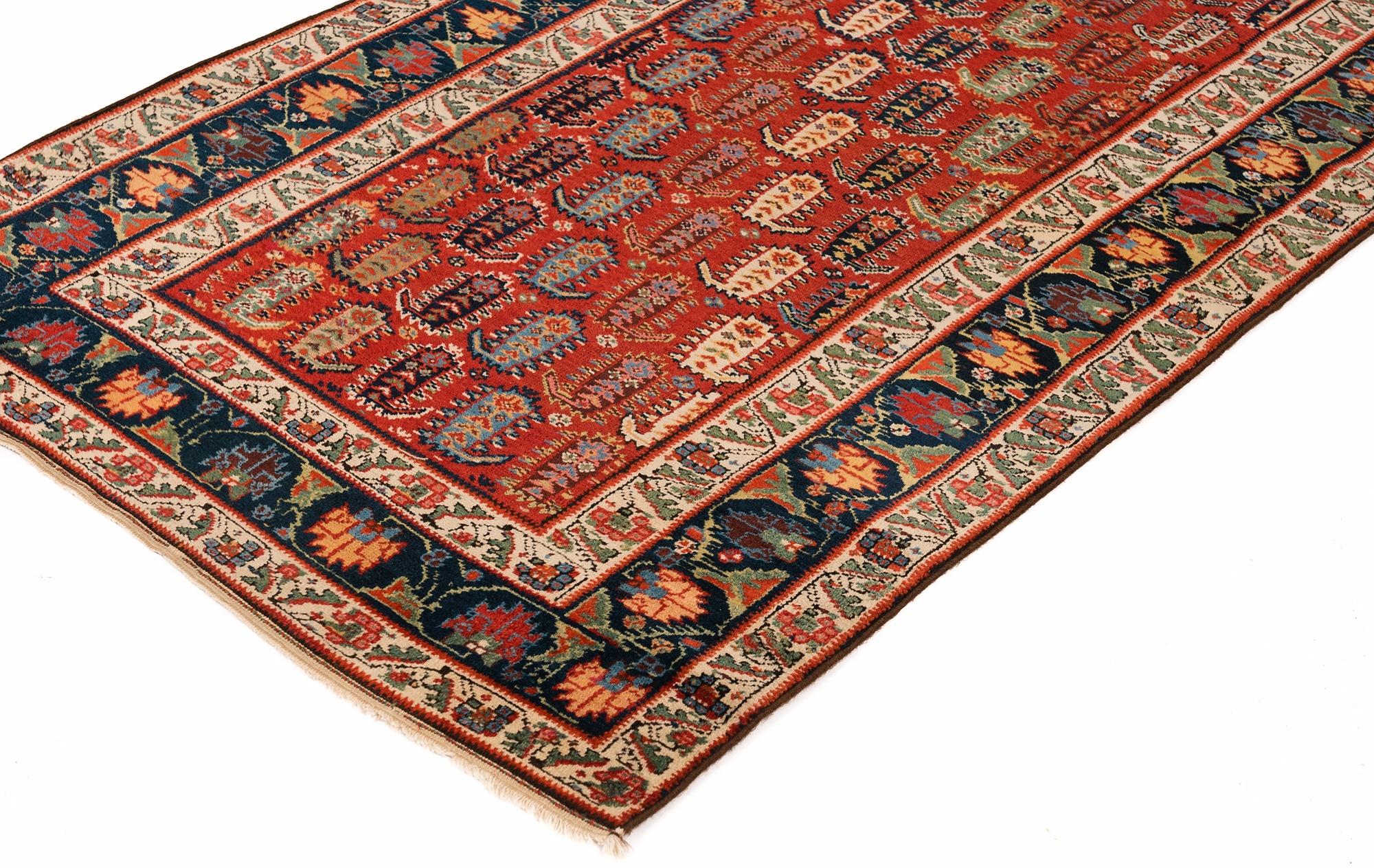 A rich cochineal red field highlights the diagonally striped boteh (paisley) motif on this magnificent Genje runner from the Armenian quarter in what is now Azerbaijan. The border is a unique ginko leaf and palmetto motif and is flanked by ivory