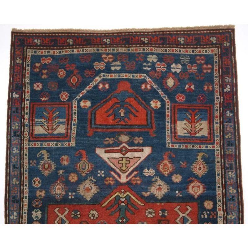 A superb example of a Caucasian prayer rug with very unusual bold design. The rug has a large central medallion in soft madder red surrounded by an indigo blue field containing boteh and floral rosettes. The rug is framed with a very narrow