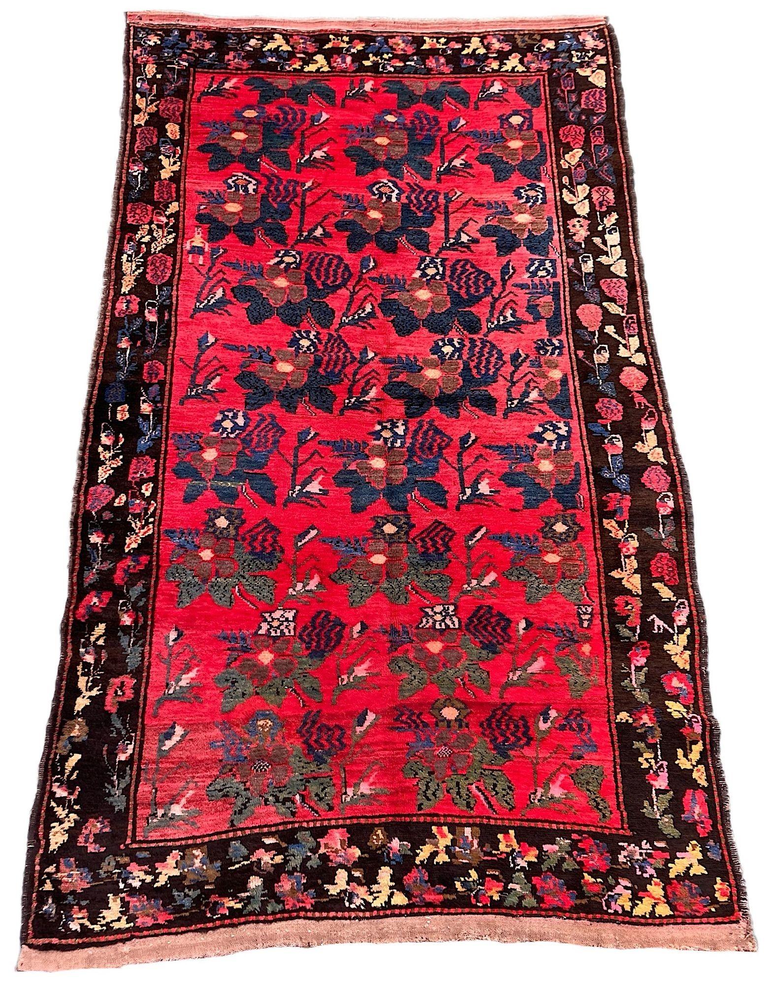 Alfombra antigua de Karabagh, tejida a mano en las montañas del Cáucaso, en el actual Azerbaiyán, hacia 1910. La alfombra presenta un diseño floral repetido en azules y verdes sobre un campo rojo intenso rodeado por un borde de carbón de flores