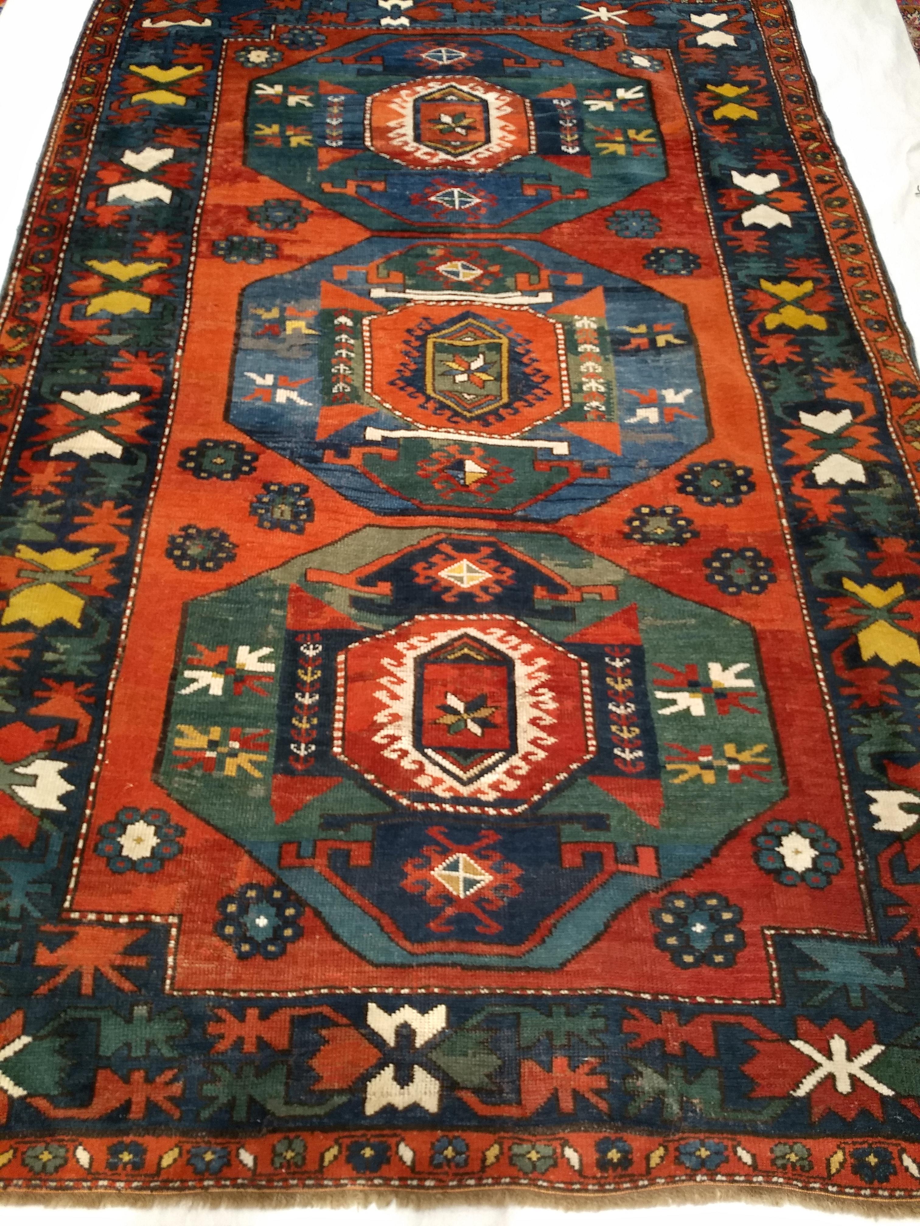 A  beautiful late 19th century Caucasian Kazak with three medallions with wonderful abrash green and blue colors throughout the design set in an antique red background.  The border has large design forms in red, yellow, green, ivory colors set in a
