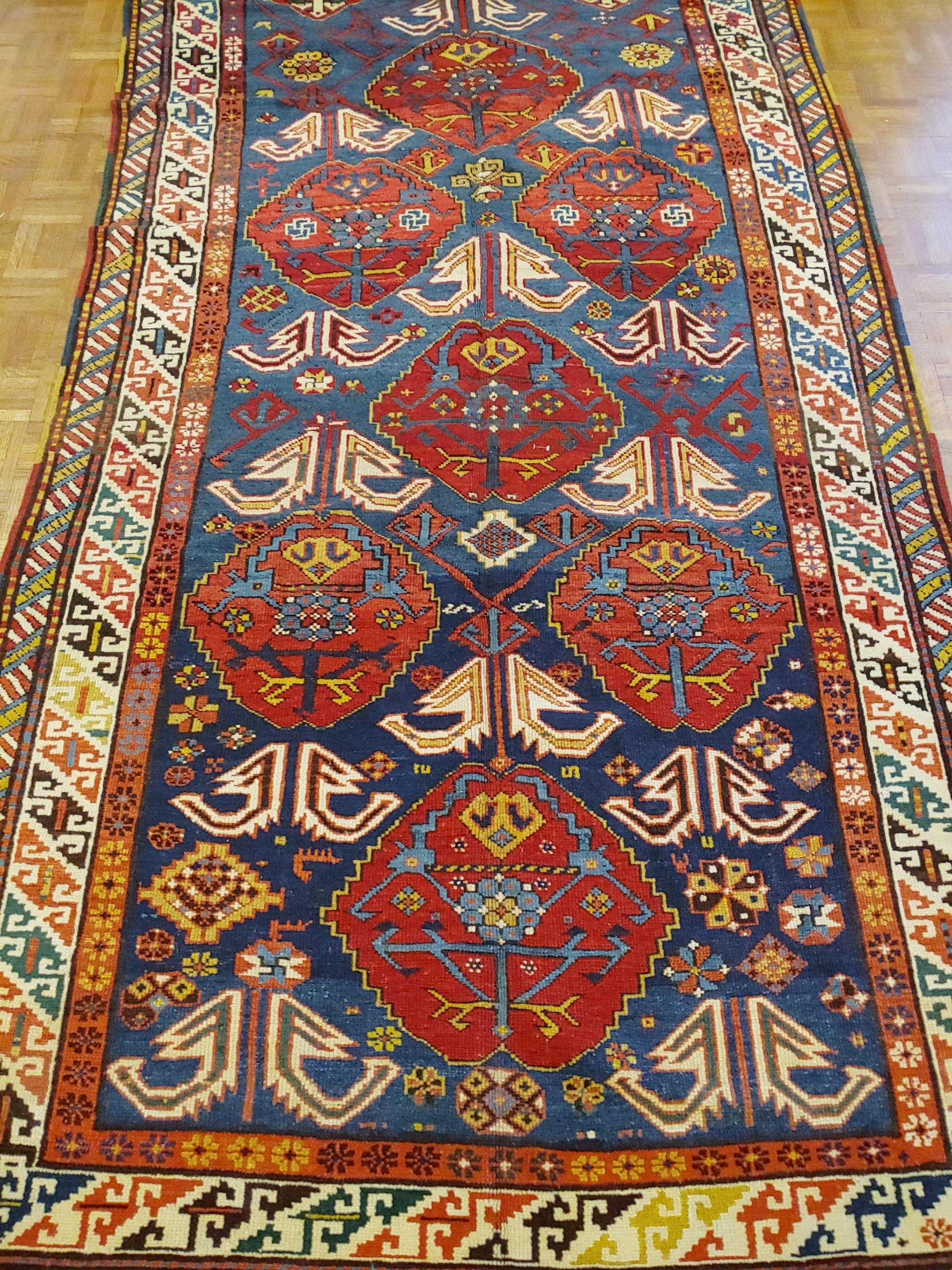 This is a unusual large Caucasian Kazak rug with the typical bold pattern on a royal blue field decorated with large stylized flower bouquets with lovely shades of ivory and red. It is circa 1910 and is a large scatter size of 5 x 9-3.