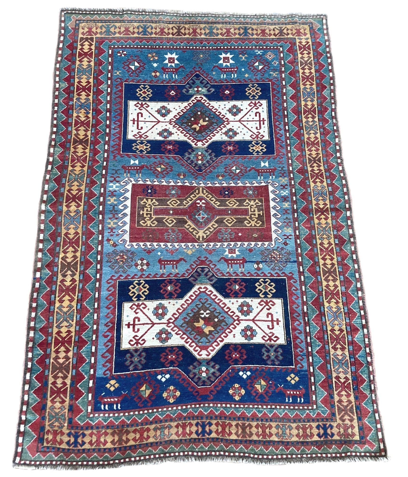 A stunning antique Kazak rug, handwoven in the Caucasus mountains of central Asia circa 1900. The design features 3 striking medallions on an indigo field and unusual gold border. Note the interesting animal figures throughout the field. Highly