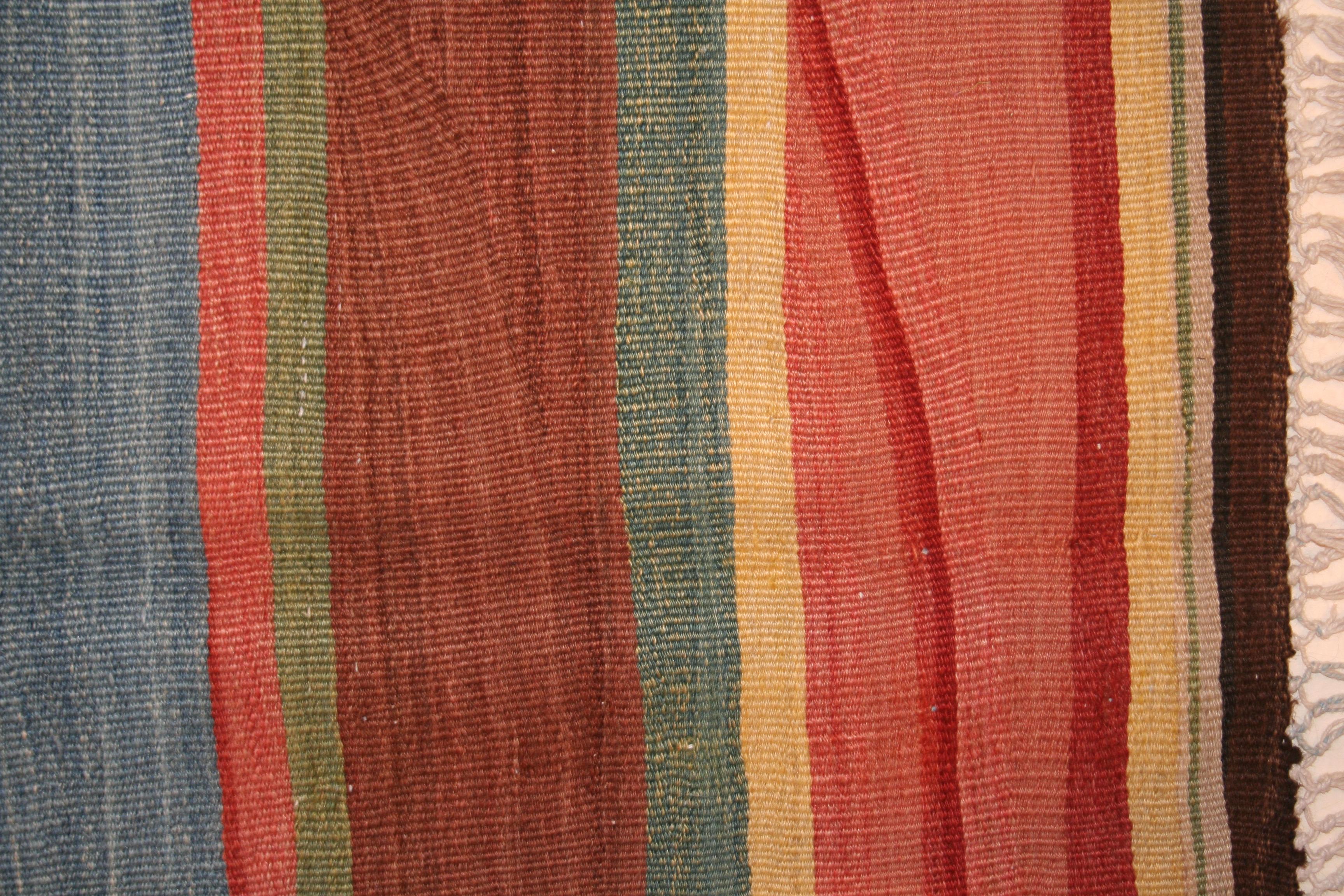 A stunning south Caucasian kilim distinguished by an horizontal arrangement of polychrome stripes of varying widths. The rich palette consists of vegetable dyes, making the wool glisten in shades that mimic nature. The sturdy texture of this