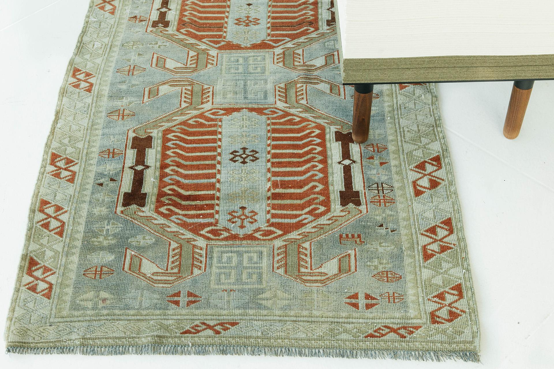 An abrash field of pale indigo and celadon, accented with brick red and deep brown, establishes an earthen palette in this tribal Caucasian piece. Features of its striking axial design include characteristic Lenkoran hooked medallions, archaic