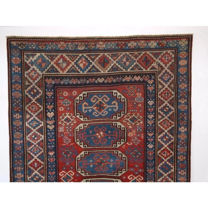 An antique Caucasian Moghan Kazak rug with a vertical row of six octagons on a soft red ground. The rug has many small filler elements to the field design and excellent traditional Moghan region border design.

The rug is in excellent condition