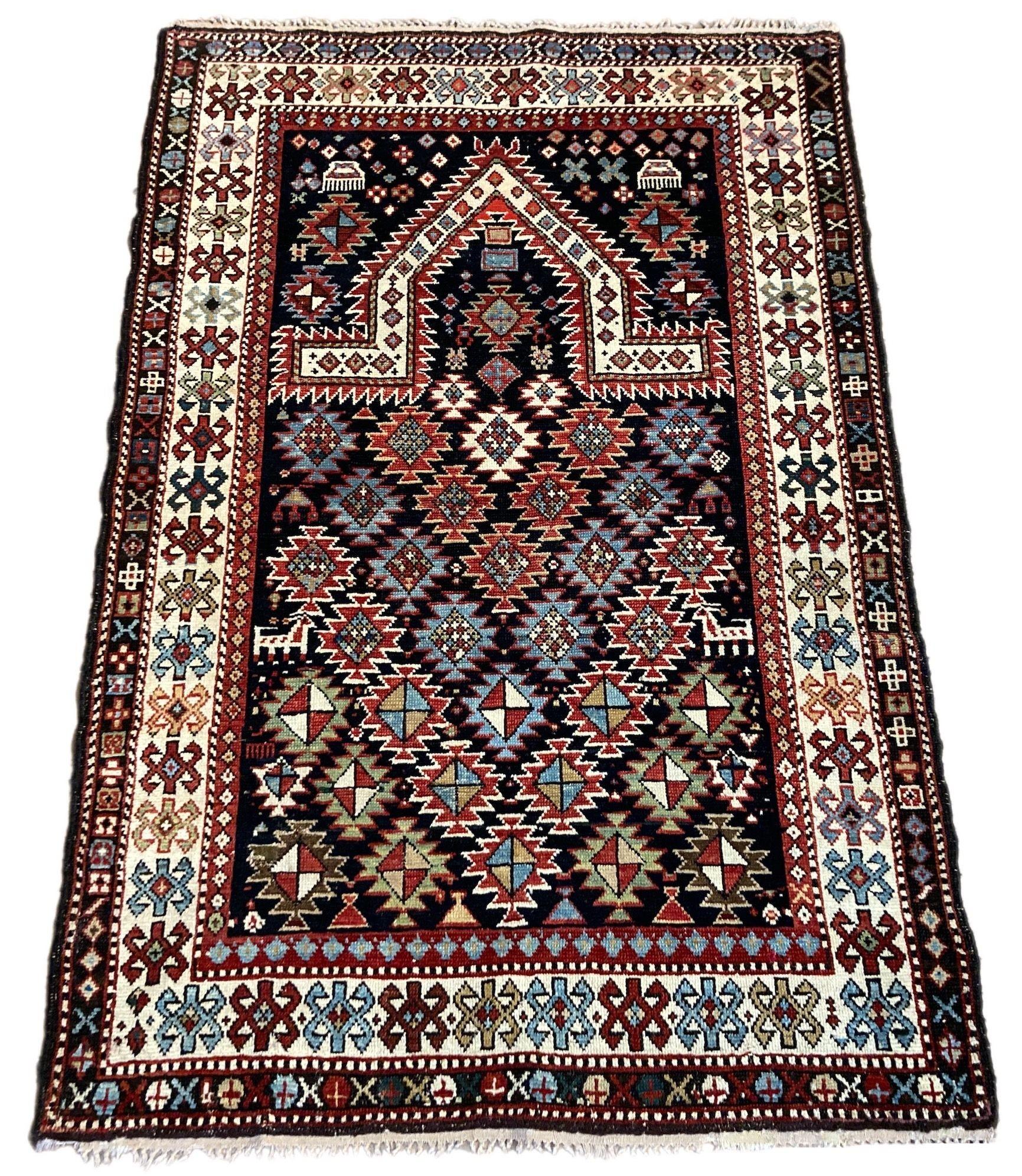 A beautiful little antique pryer rug, handwoven in The Caucasus mountains, possibly in Dagestan, circa 1900. It features a traditional Mihrab design on a deep indigo lozenge field with an ivory border. Note the small animal figures in the field.