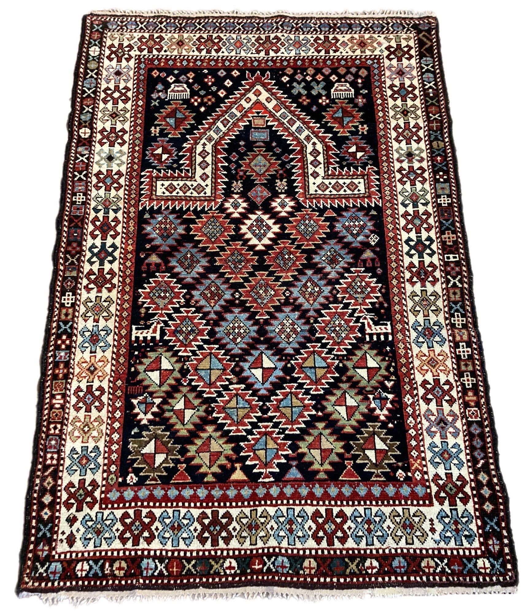 Ein wunderschöner kleiner antiker Fransenteppich, handgewebt im Kaukasus, möglicherweise in Dagestan, um 1900. Es zeigt ein traditionelles Mihrab-Muster auf einem tief indigoblauen Rautenfeld mit elfenbeinfarbener Bordüre. Beachten Sie die kleinen
