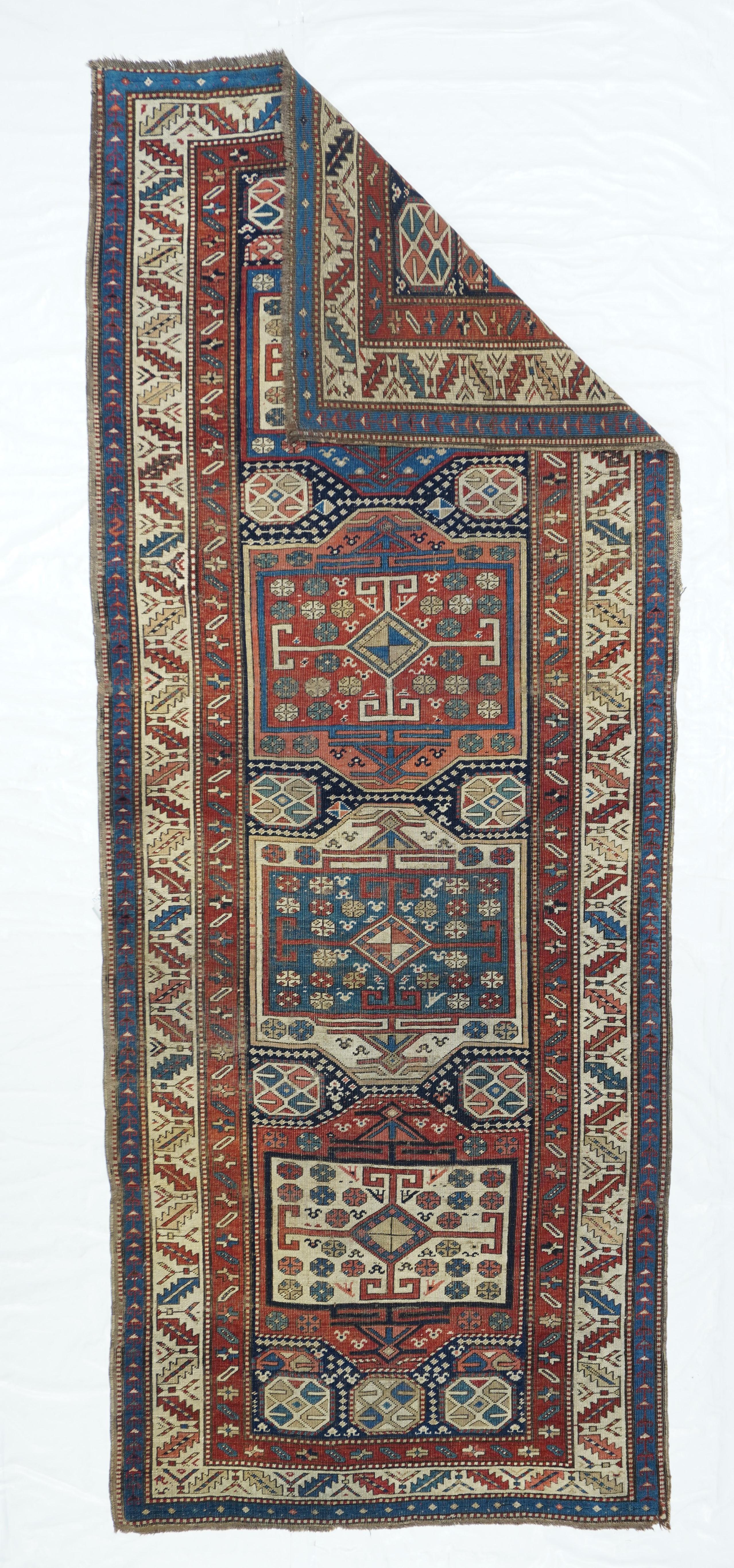 The navy field of this all wool construction, leathery handle, east Caucasian long rug (kellegi) hosts four squarish cartouches in red, ivory, dark blue- green and burnt salmon. Lozenges with long arms decorate each panel’s centre. Smaller octagons