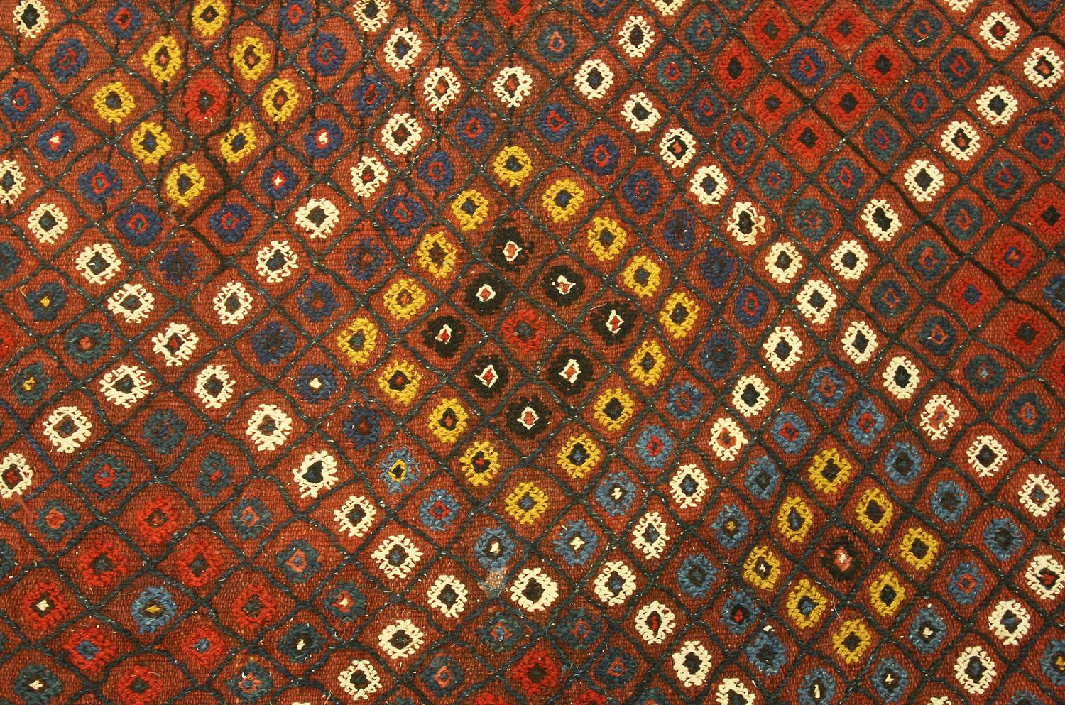 An antique Verneh small carpet, South Caucasus. The field with overall multicolored small rosettes in a lozenge shape lattice. In polychrome-shaped baton and lozenge border between running-dog and barber-pole stripes. Similar design rust skirt at