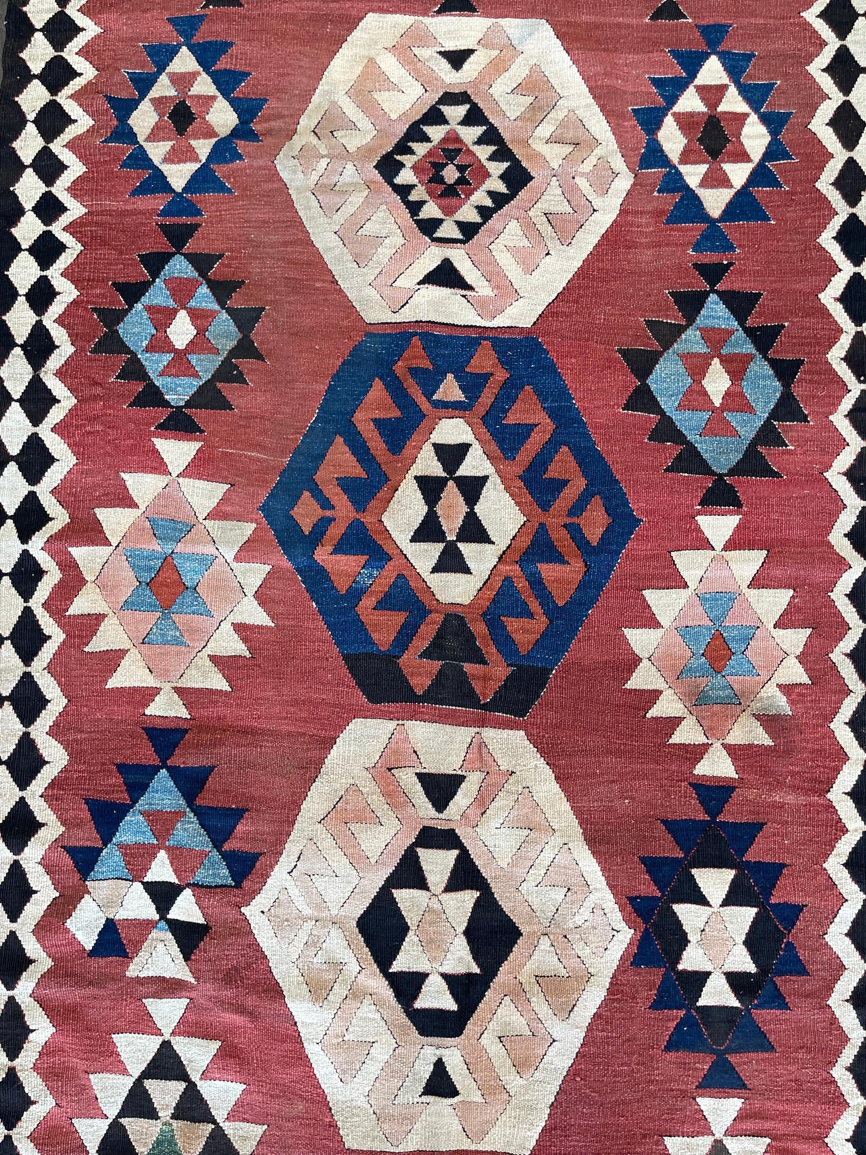 A beautiful antique Caucasian flat weave Kilim attributed to the town of Shirvan in the caucasus mountain featuring a soft salmon/orange field decorated by three hexagon shaped medallions one in blue and two in beige colors, surrounded by forteen
