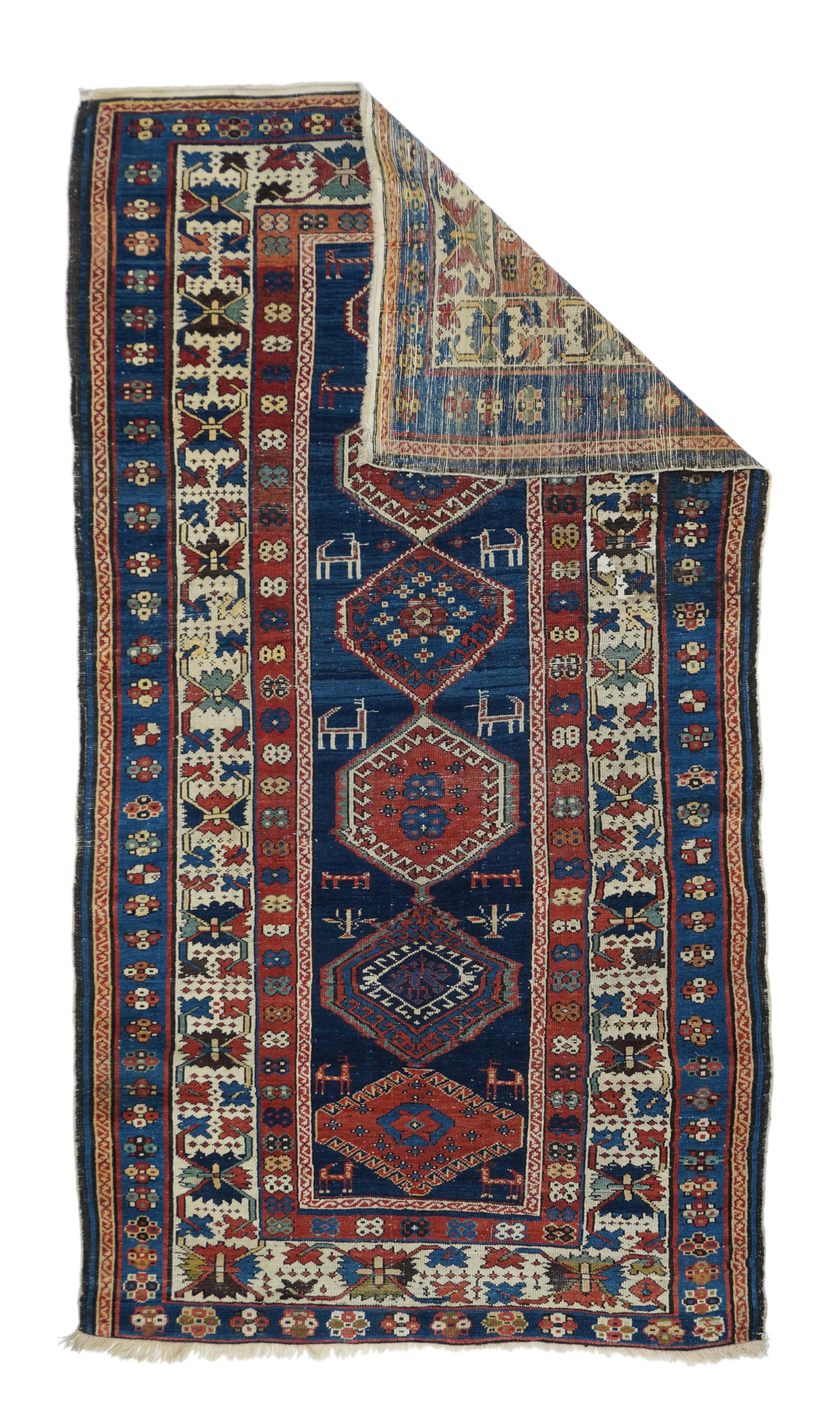This elongated east Caucasian scatter presents an abrashed, deep sapphire field centred by a pole medallion of six red and cream hexagons with hooked sub-hexagons, and flanked by pairs of rustic animals. Main ivory ground 