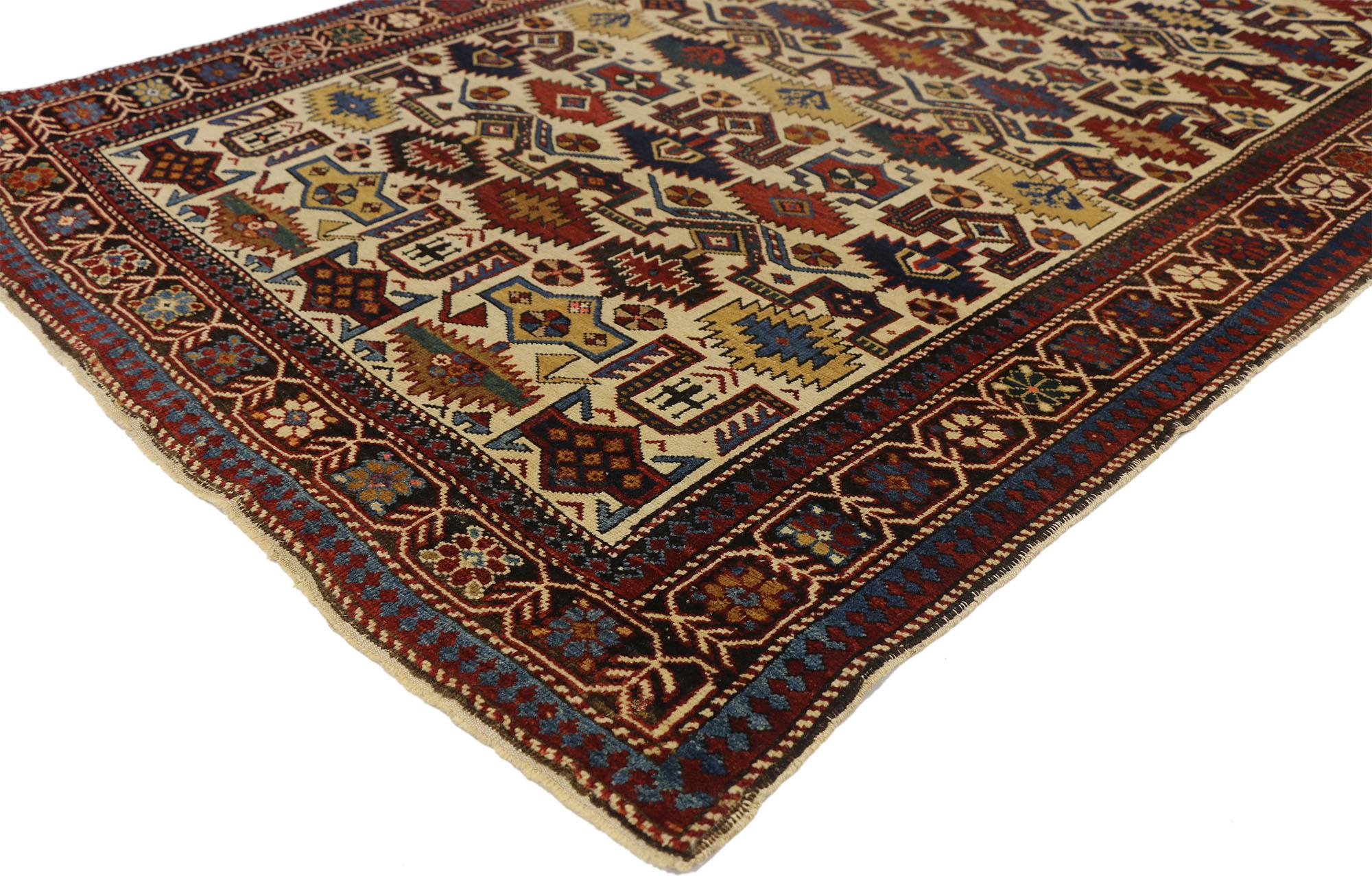 This antique Caucasian Shirvan rug with modern tribal style features an allover geometric pattern on a vanilla beige field surrounded by a simplistic floral border. The color palette consists of red, blue, ivory-beige, mustard yellow, rust, teal,