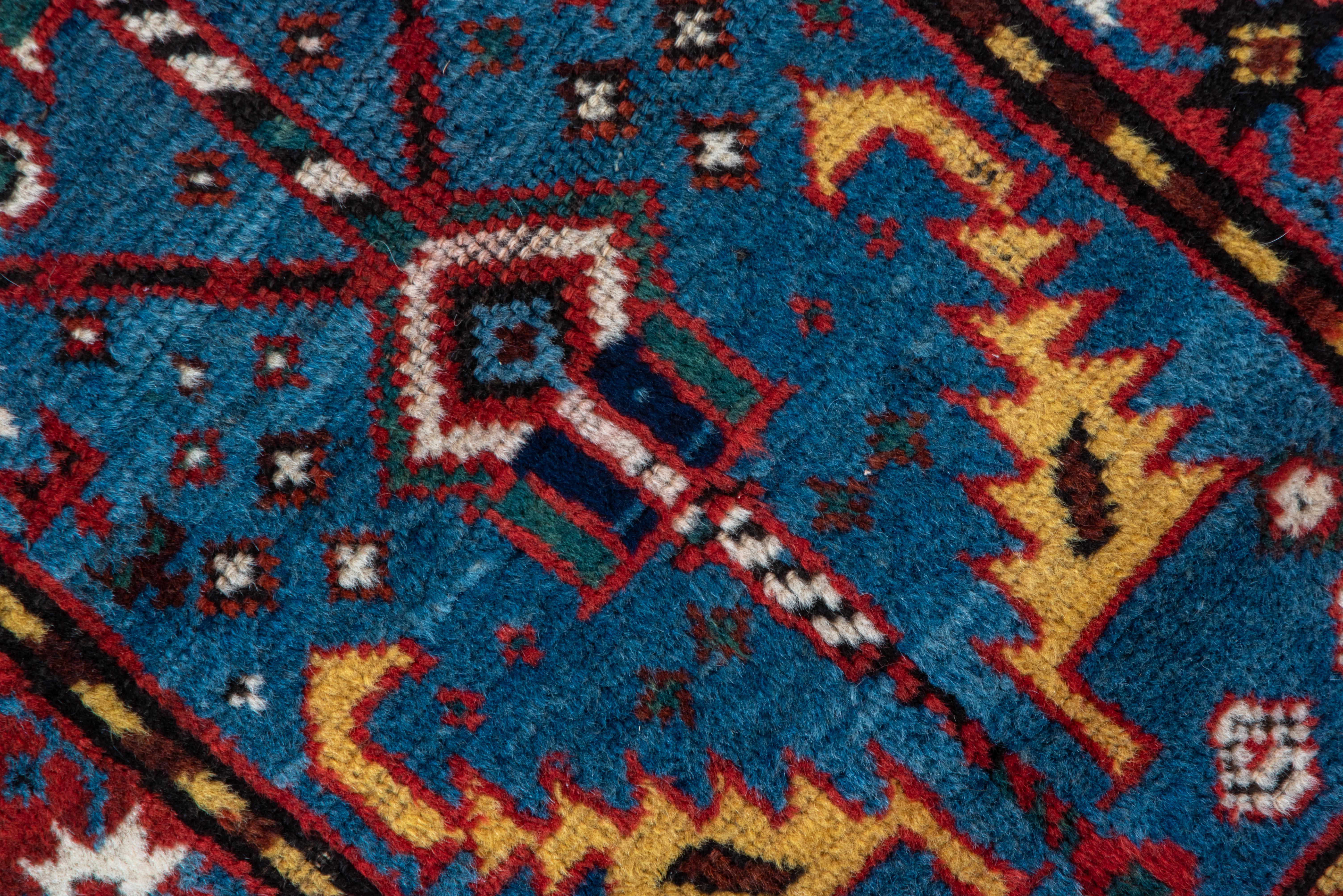 This very versatile small South Caucasian runner shows a brisk cerulean blue field featuring a vertical repeating leaf and flower one-way pattern with accents in straw, chocolate, green and ecru. Off-white main border of joined 
