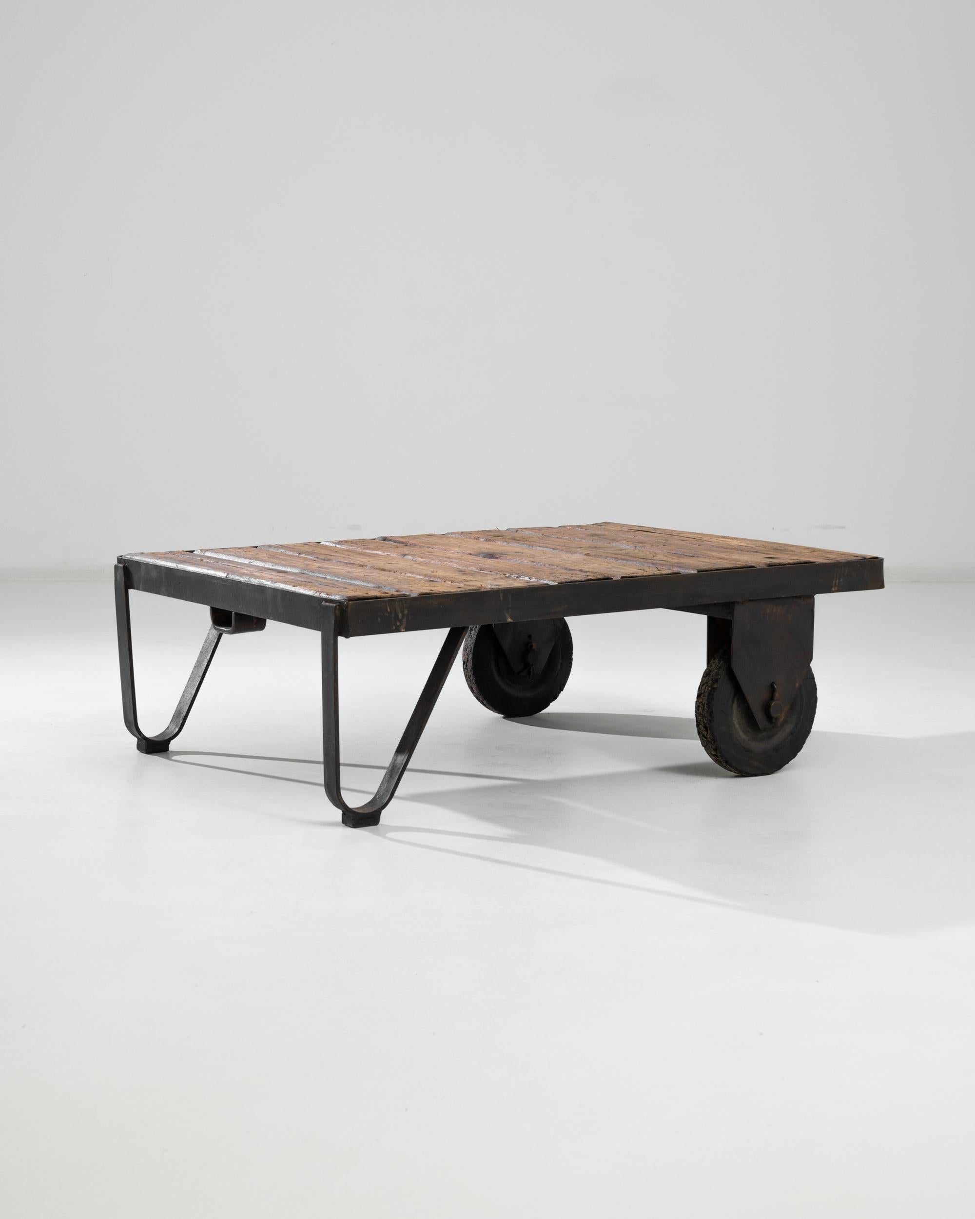 A metal coffee table on wheels from Central Europe, produced during the 20th century. Eight stretched out horizontal planks mounted in black metal frame resting on two “U” shaped metal supports and a pair of wheels—giving it the functional