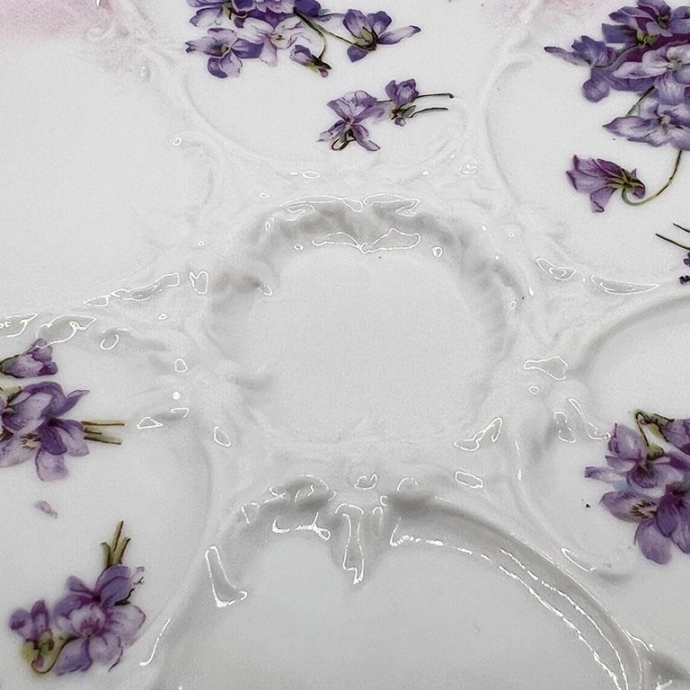 A beautiful purple and pink floral oyster plate. This piece will be a great addition to a hanging oyster plate gallery wall. It has 7 wells, with 6 around the perimeter, and one small floral wreath motif one in the middle. The edges are scalloped