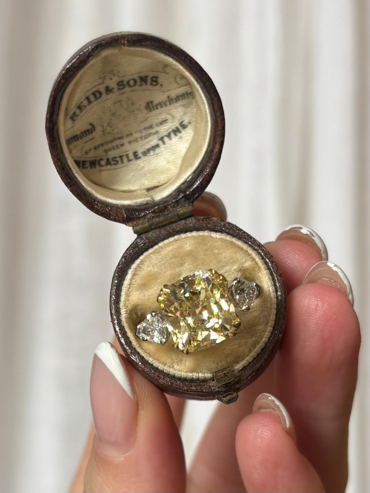 A beautiful antique 4.97ct old cushion cut diamond three stone ring set in 18k yellow gold and platinum.

The ring is centrally set with a stunning antique old cushion cut diamond which is certified as a natural fancy light yellow. The diamond is