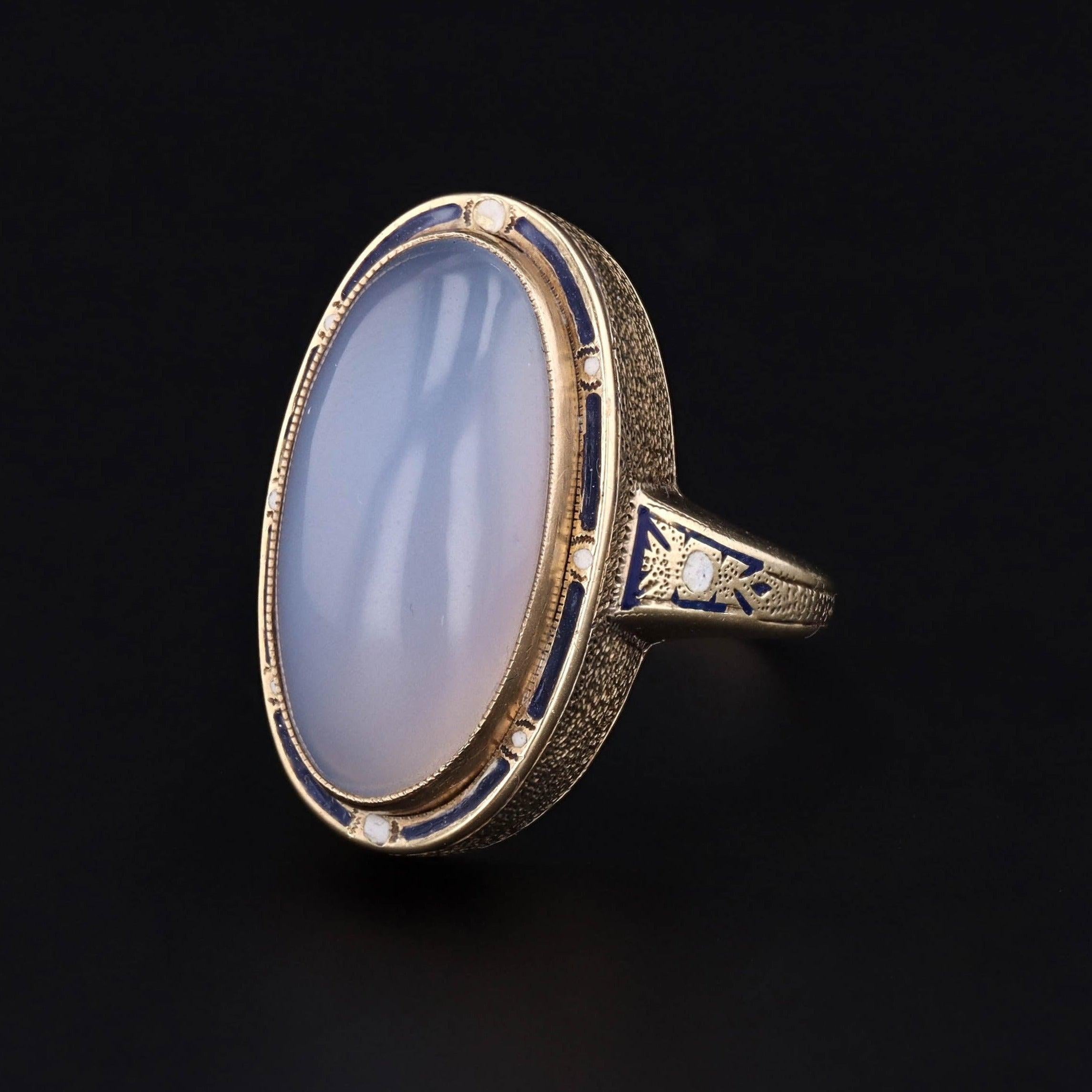 Un anello in calcedonio blu con smalto blu e bianco.

Questo splendido anello presenta un etereo calcedonio cabochon a cupola che misura 20 mm da nord a sud e 10 mm da est a ovest. Il calcedonio è montato in oro 14k e la pietra è incorniciata da