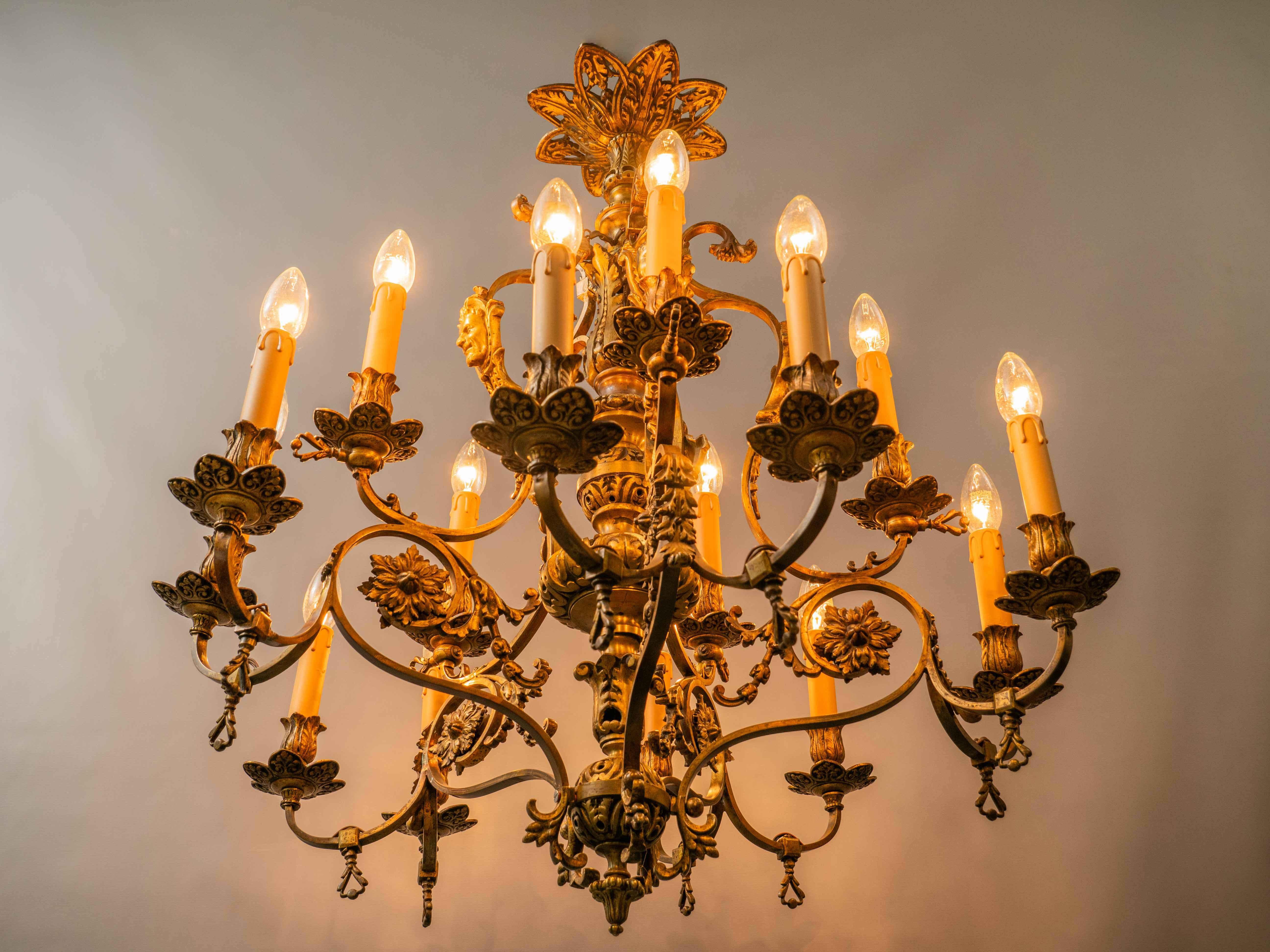 Originally a gas chandelier - the chandelier still has its original shut-off taps. Five main arms, from which develop three smaller ones with bulbs. The upper supporting arms are decorated with mascarons, and the entire chandelier with floral decor.