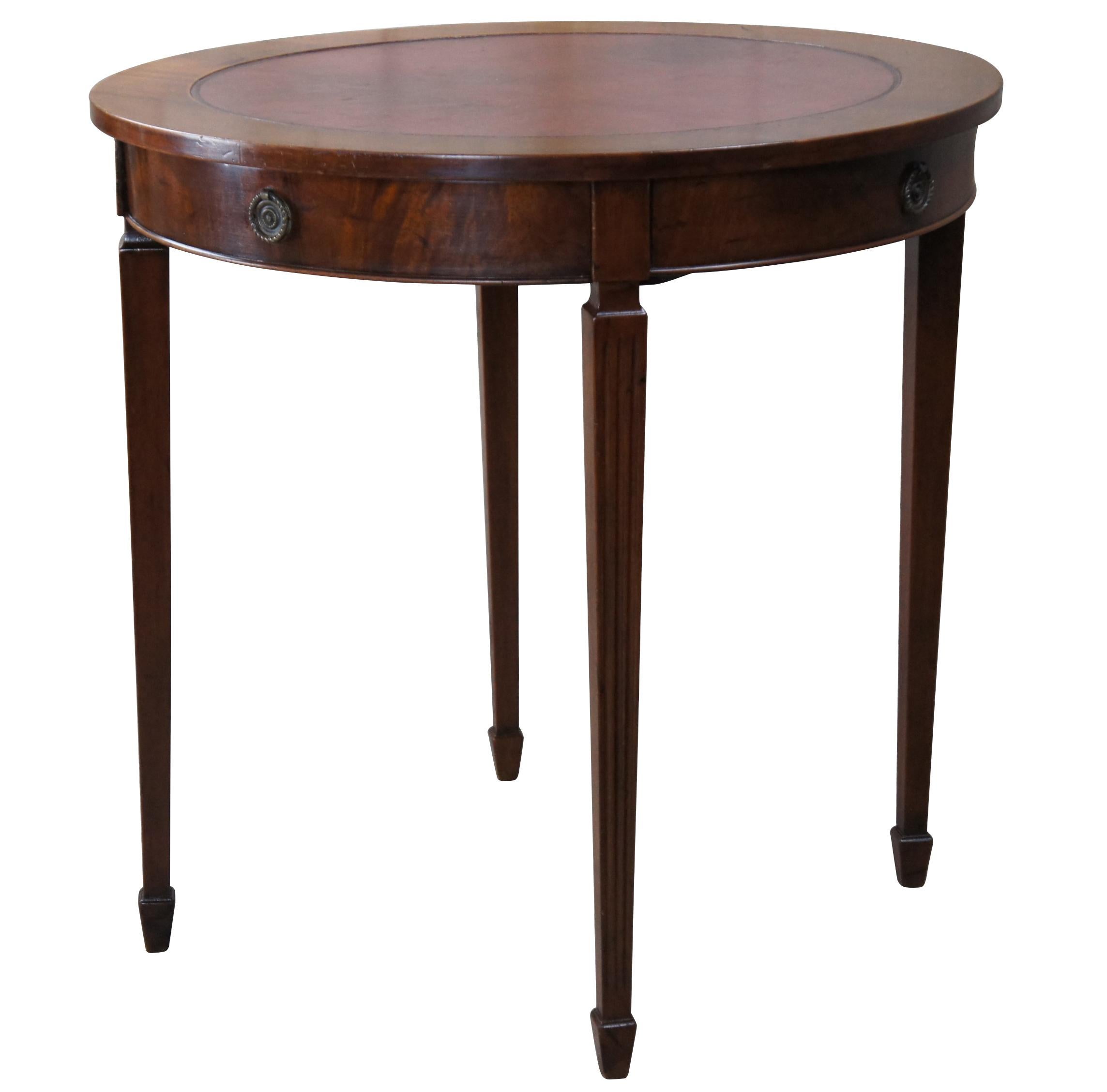 An antique Sheraton style table made by Charak for The H. & S. Pogue Company of Cincinnati, circa 1936. Features a round form with inset red leather top over a flame mahogany frieze with dovetailed drawer and brass hardware. The table is supported