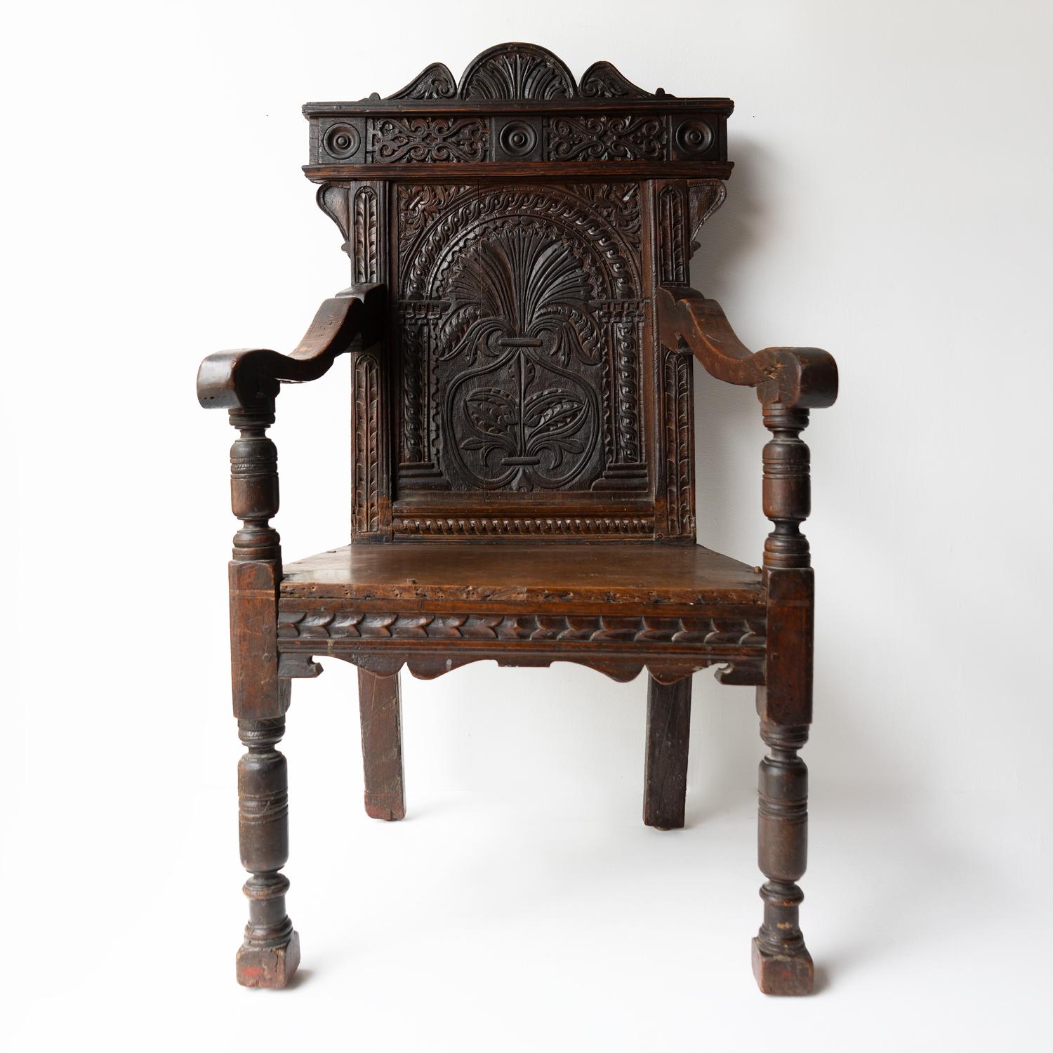 Early English Antique Armchair

A handsome chair with turned front supports a carved back panel, shaped down swept arms and a plank seat.

Naturalistic carving with geometric shapes and foliate motifs surrounding a central version of the Tree of