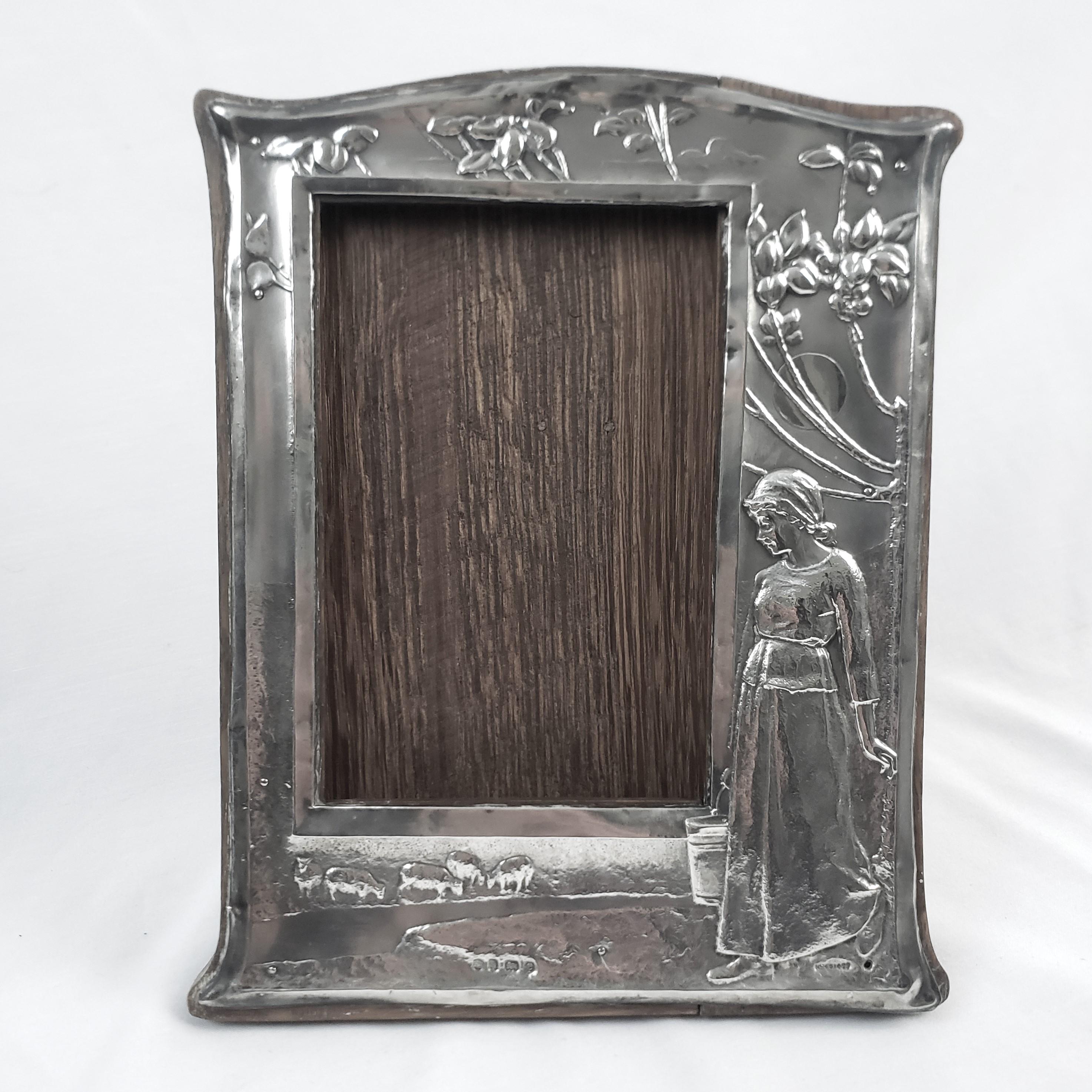 This antique picture or mirror frame was made by the well known Charles S. Green Company of England in approximately 1907 in the period Arts and Crafts style. The front of the frame is composed of sterling silver with repousse decoration depicting a
