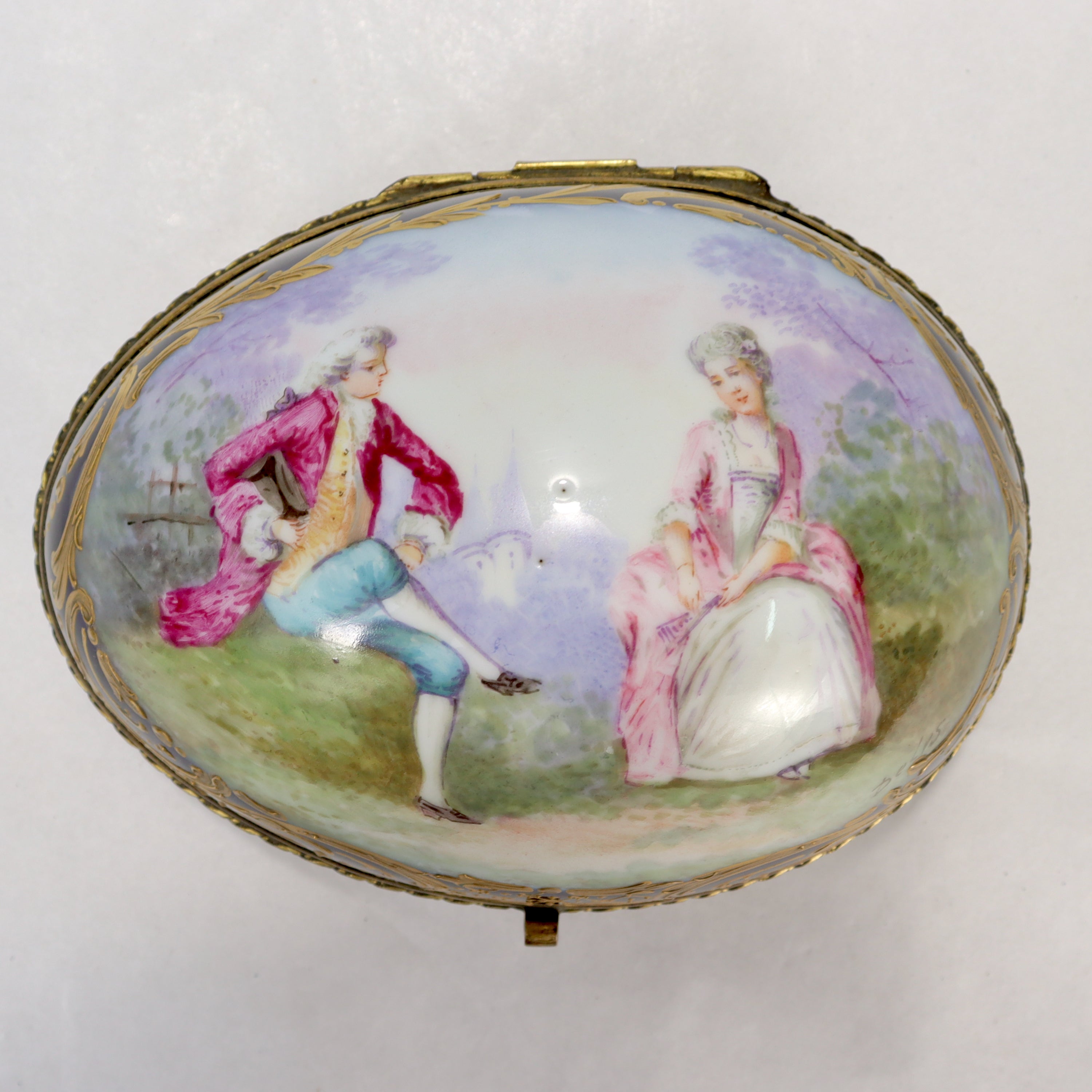 A fine, signed antique French porcelain dresser box. 

In a rare oval or egg form. 

Decorated with a cobalt ground, signed hand painted scene with lovers in a garden, and rich gilding throughout.

Signed Delys.

Marked to the base with a
