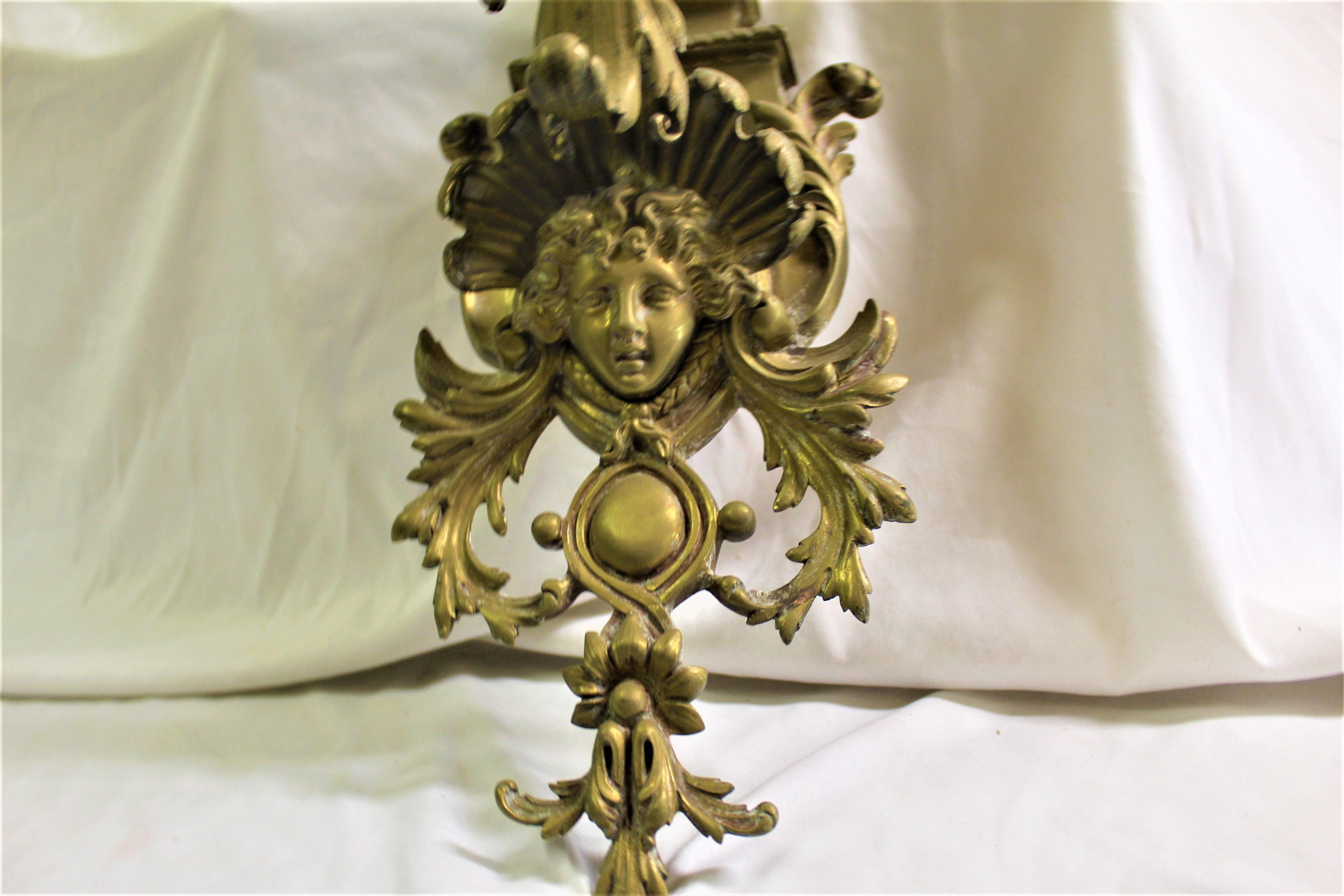 A large early cherub sconce cast in solid brass with 4 arms and French wired at some time . The bottom has Lady face cast into the scrolling Acanthus leaf's all around . At the top there is a Flame finial . This is over 35