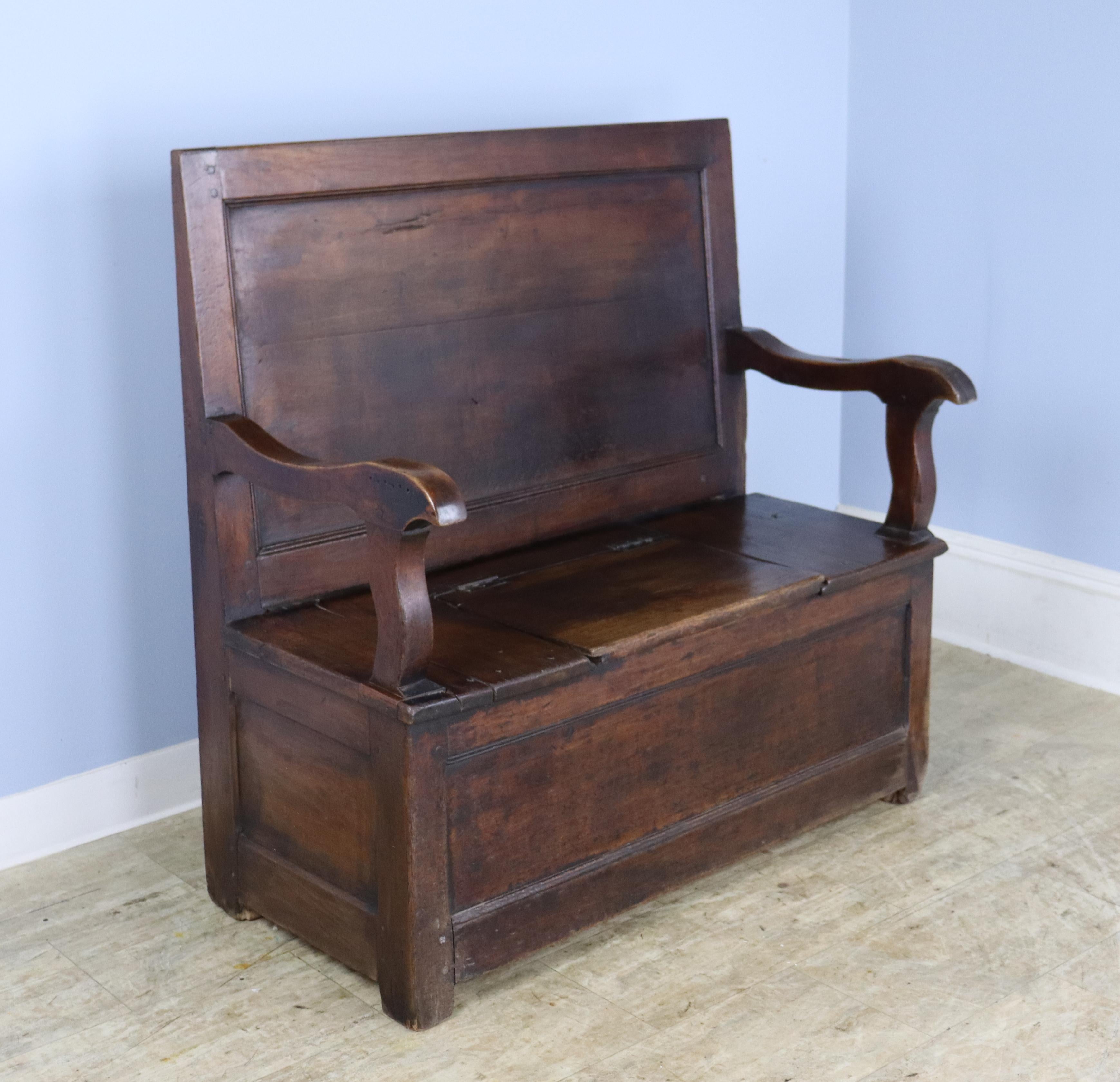 A chunky, handsome cherry fireside seat from France.  Wonderful grain and patina with charming carved arms and sloped backrest. Small flip-top in the seat with original hinges provides storage. Would work well in a mud room or front hall.  There is