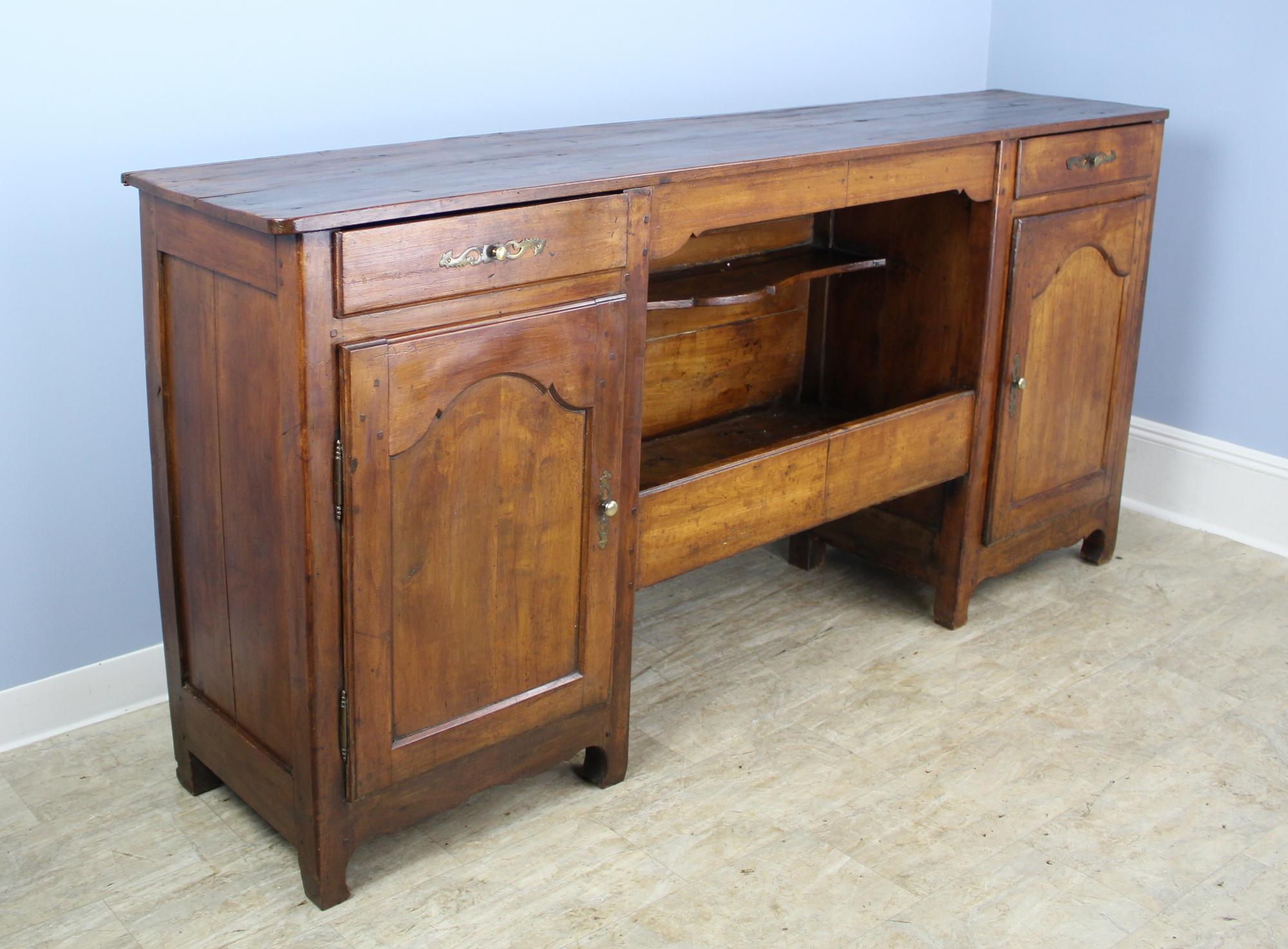 A large cherry enfilade or buffet in warm cherry with several interesting features. The open centre has a decoratively carved shelf and an enclosed lower storage area for utility. The cupboards on either side have two non-adjustable shelves, and the