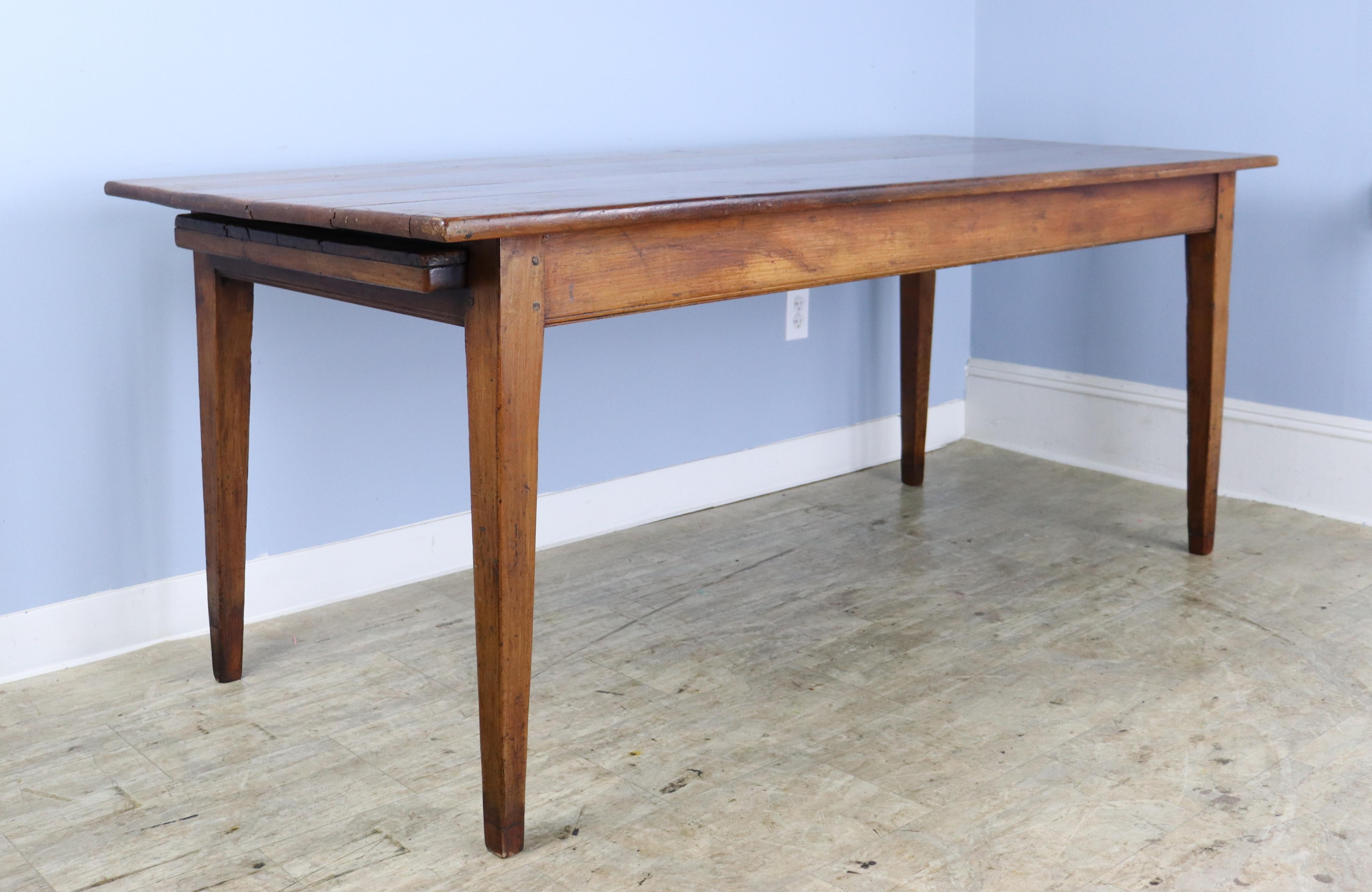 A solid country farm table in warm cherry. The wood has very nice grain, patina and color, and the table's charming drawer and beautiful bread slide add an eye catching design note. Classic tapered legs, well pegged at the base. There are some small