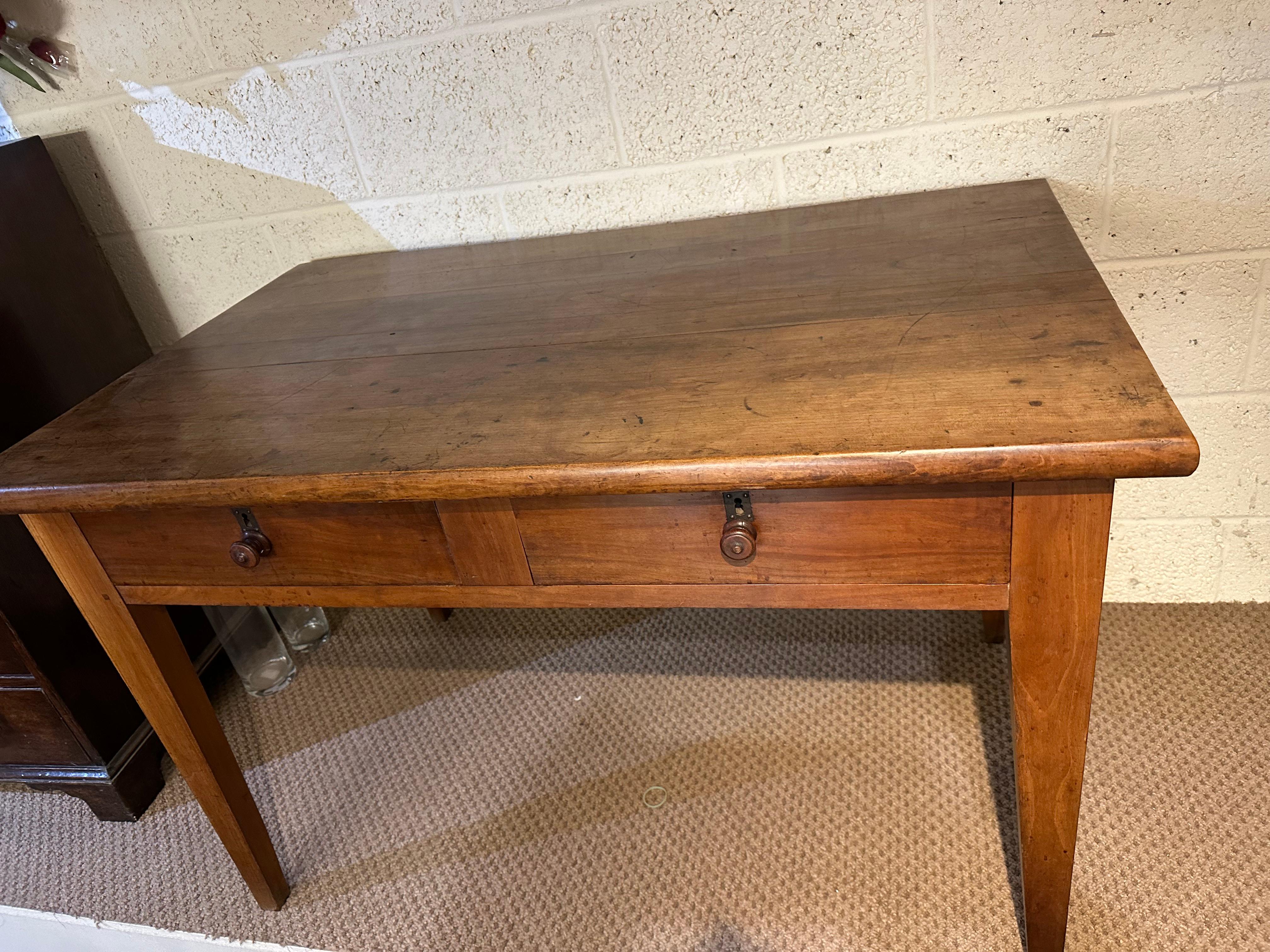 The 19th Century cherry two drawer desk on tapered legs is a remarkable piece of furniture. It features a beautiful patination and colour showcasing the natural aging and wear that adds character and charm to the desk. The desk stands on sturdy