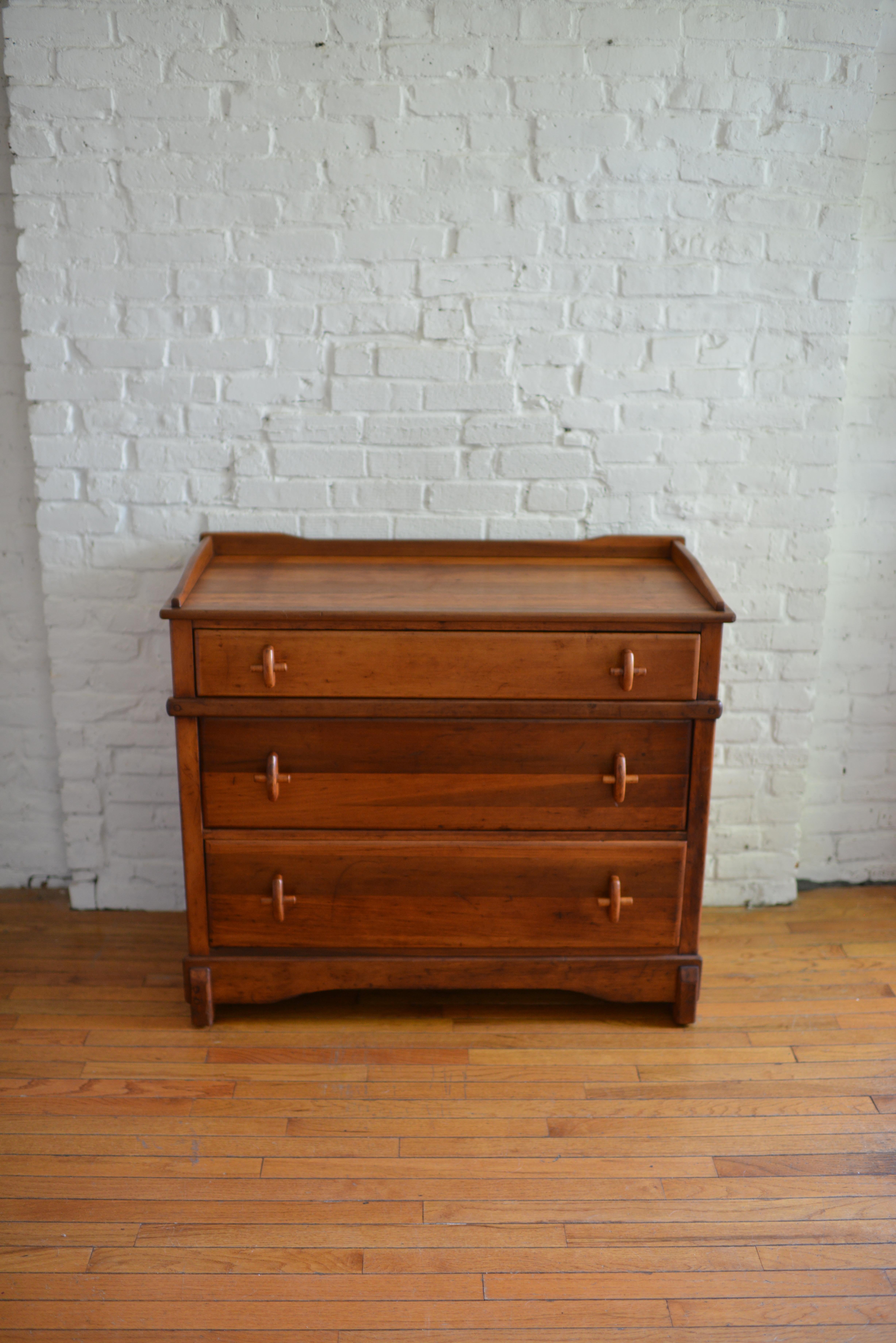 Exquisite early 20th century solid wood chest of drawers. This solidly constructed piece features beautifully turned cross pull handles and dovetail joints. The piece has three generously-sized drawers, block feet and a simply carved apron front.