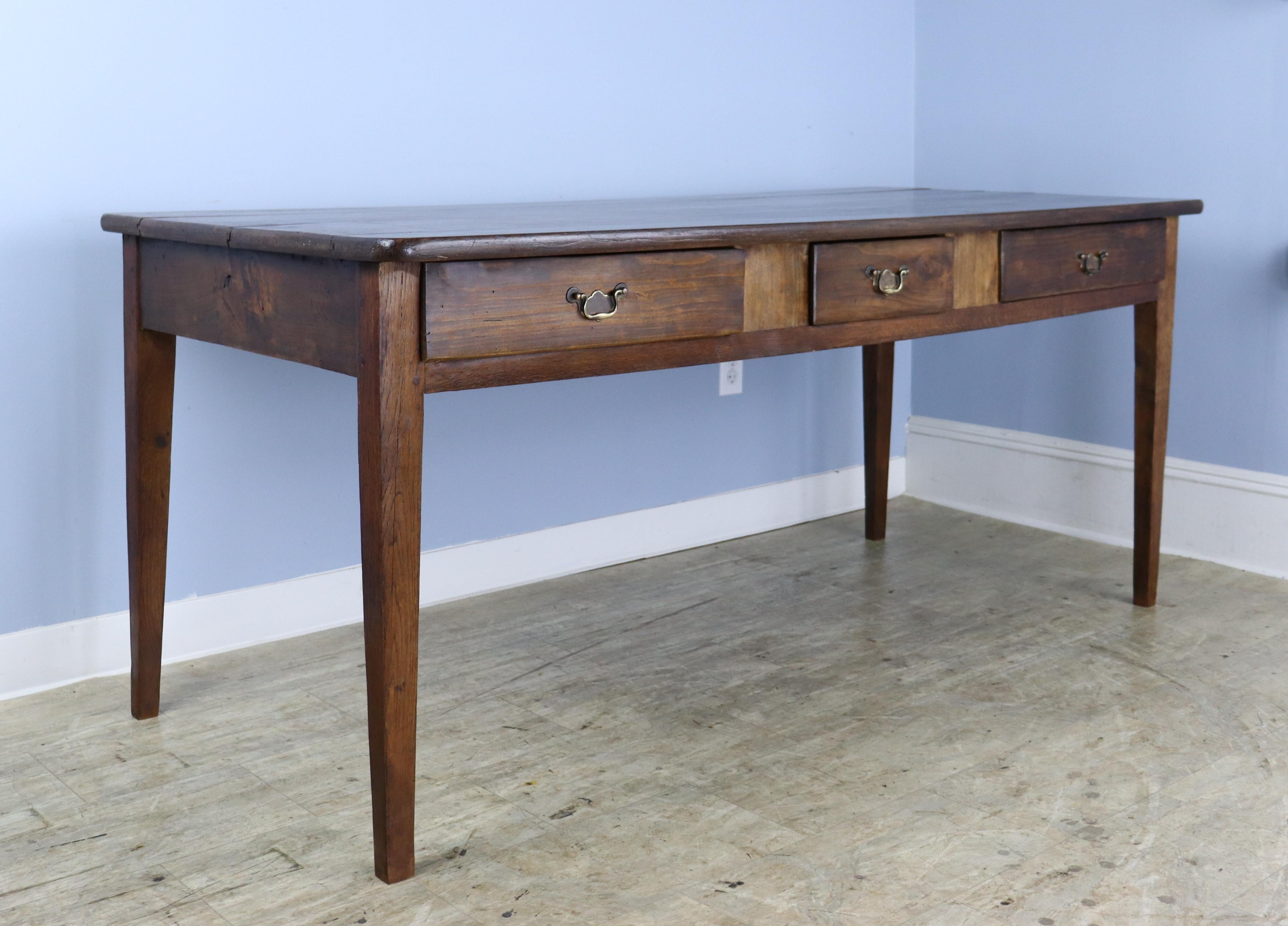 A smaller farm table or large desk with three drawers in rich chestnut. The top has rounded corners and lovely color and grain. Tapered legs are well pegged at the apron. There are 66 inches between the legs on the long side, and the apron height is