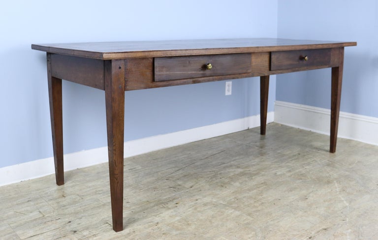 A sleek French chestnut farm table in a good 6-8 person size. Very good chestnut color and grain and two roomy, clean drawers for napkins or other dining needs. Apron height of 25 inches is good for knees and there are 67.5 inches between the legs