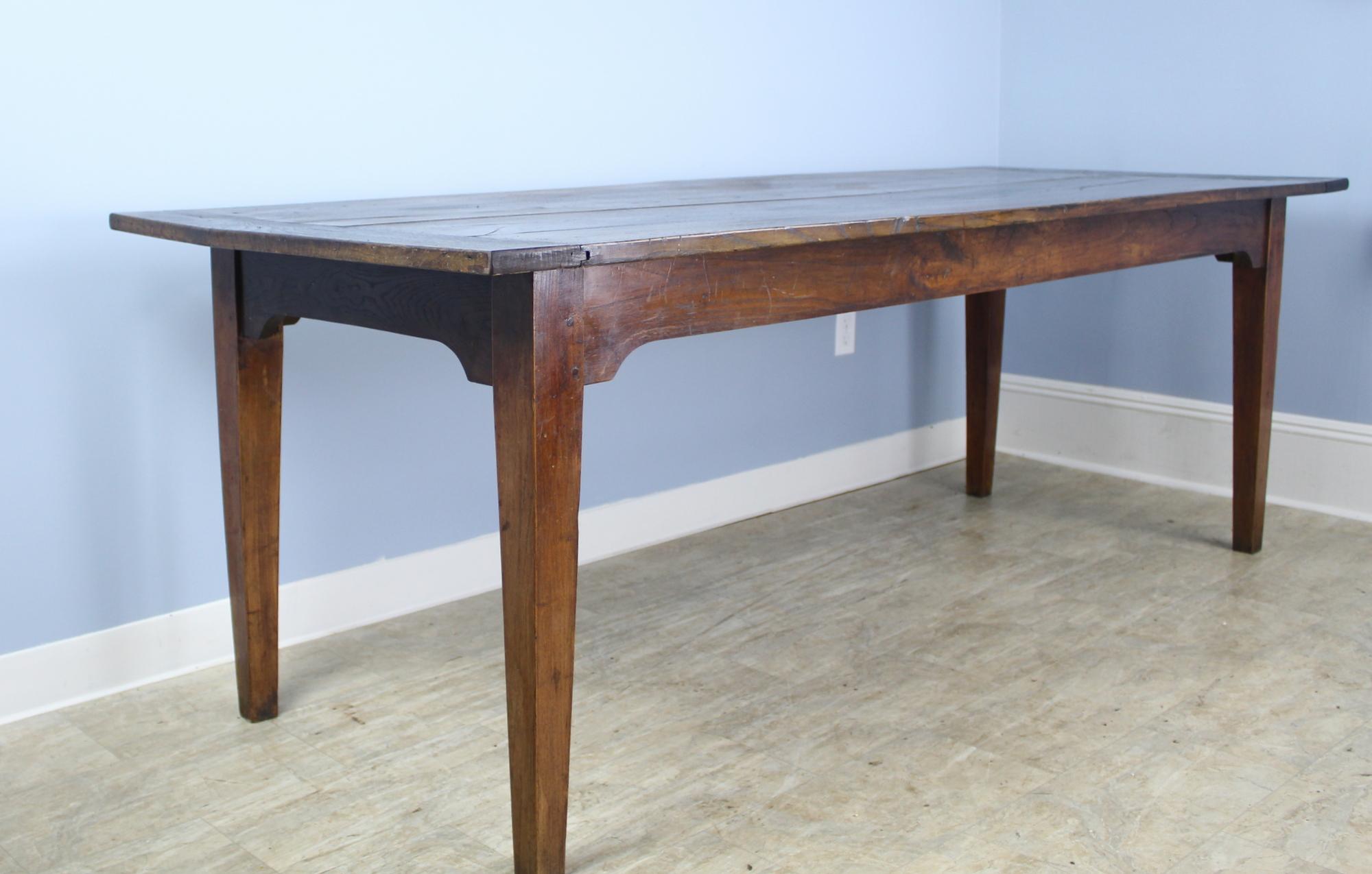A Classic dark chestnut French farmhouse table. Slender tapered legs positioned near the end of the top to maximize seating between the legs. Color is a rich warm chestnut with a good, aged, patina. Breadboard ends on the top. Apron height is a good