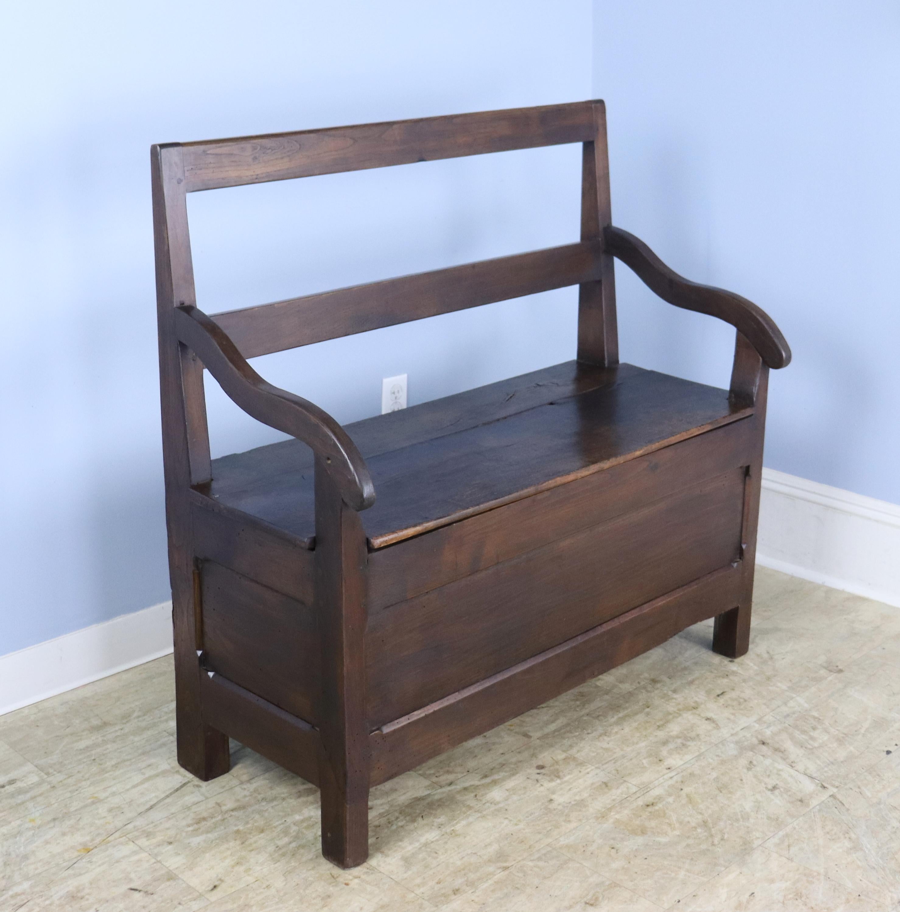 A handsome chestnut bench with charming sloping arms and a lift off lid with good storage.  The chestnut hads rich color and fine patina.  There are some areas of old wear, shown.  Would be right in a hallway or mudroom, or for any occasional