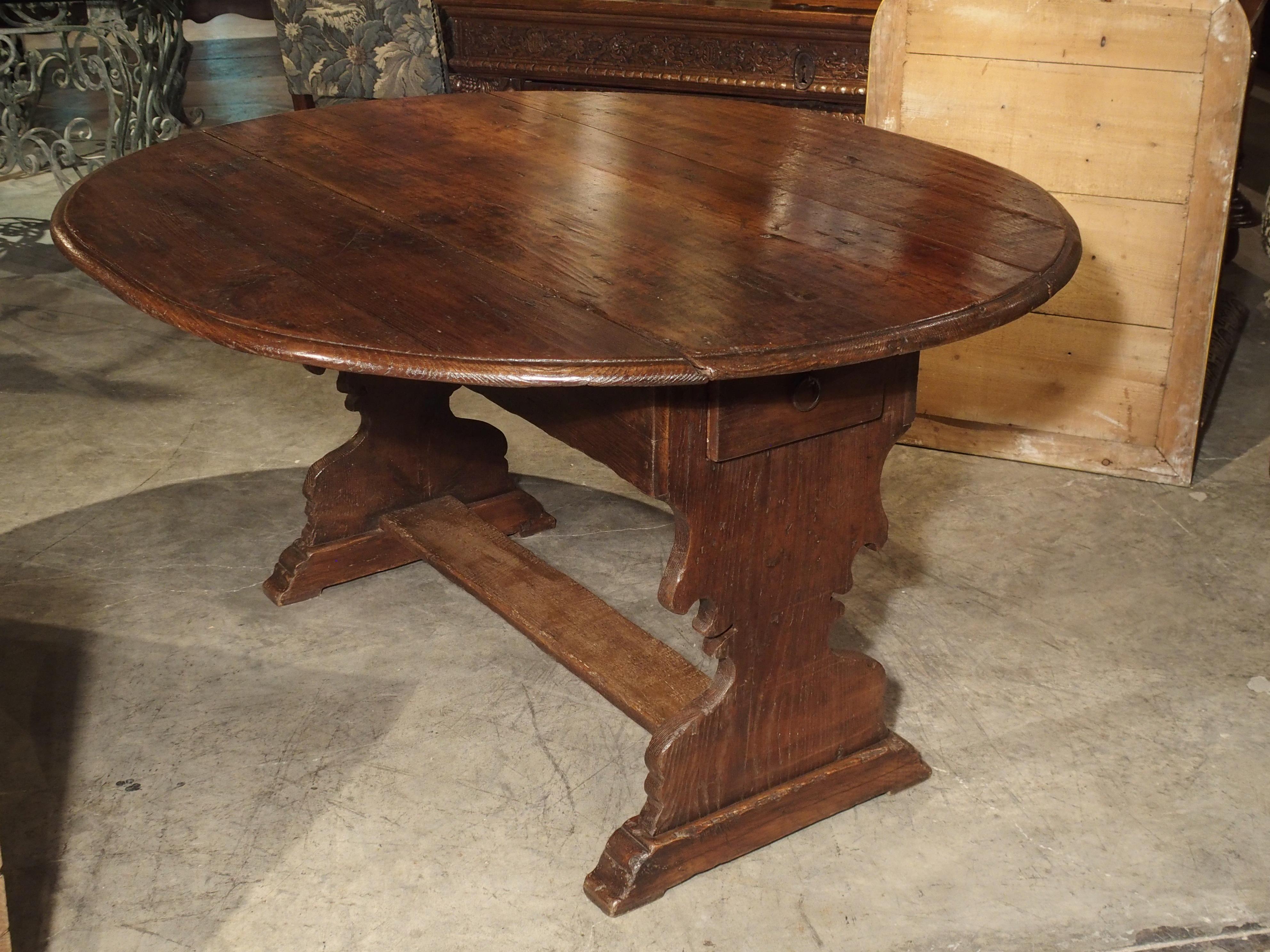 This antique chestnut wood, drop leaf table is from Italy, circa 1780. It has two drop leaves on either side of the center plank. The plank has an apron with deep drawers on either end, and the apron has shaped wooden holders to support the leaves.