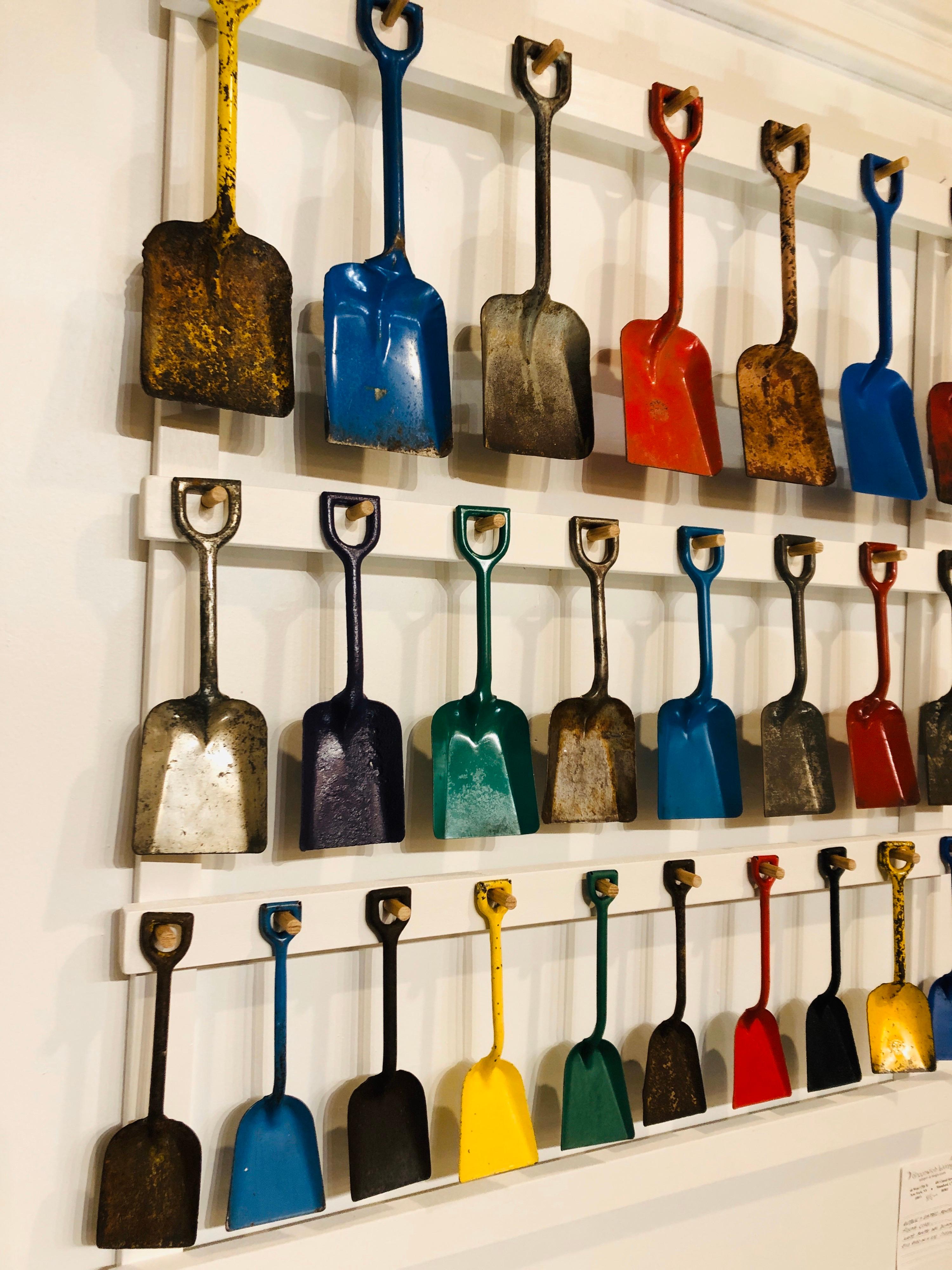 A custom mounted display of 25 antique child's toy pressed metal beach sand shovels in various sizes and colors. Dating from 1940s-1950s. Shovels ranging in size from 8 1/2 to 12