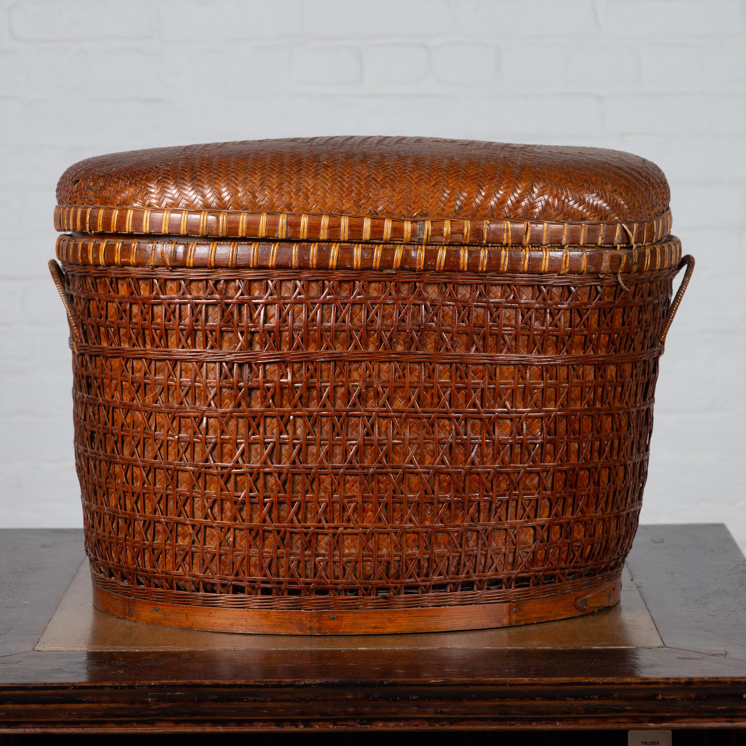 A Chinese antique Qing Dynasty oval-shaped rattan basket from the 19th century, with lid and handles. Born in China during the 19th century, this rattan basket features an oval lid, adorned with discreet geometrical motifs. The lid sits above a