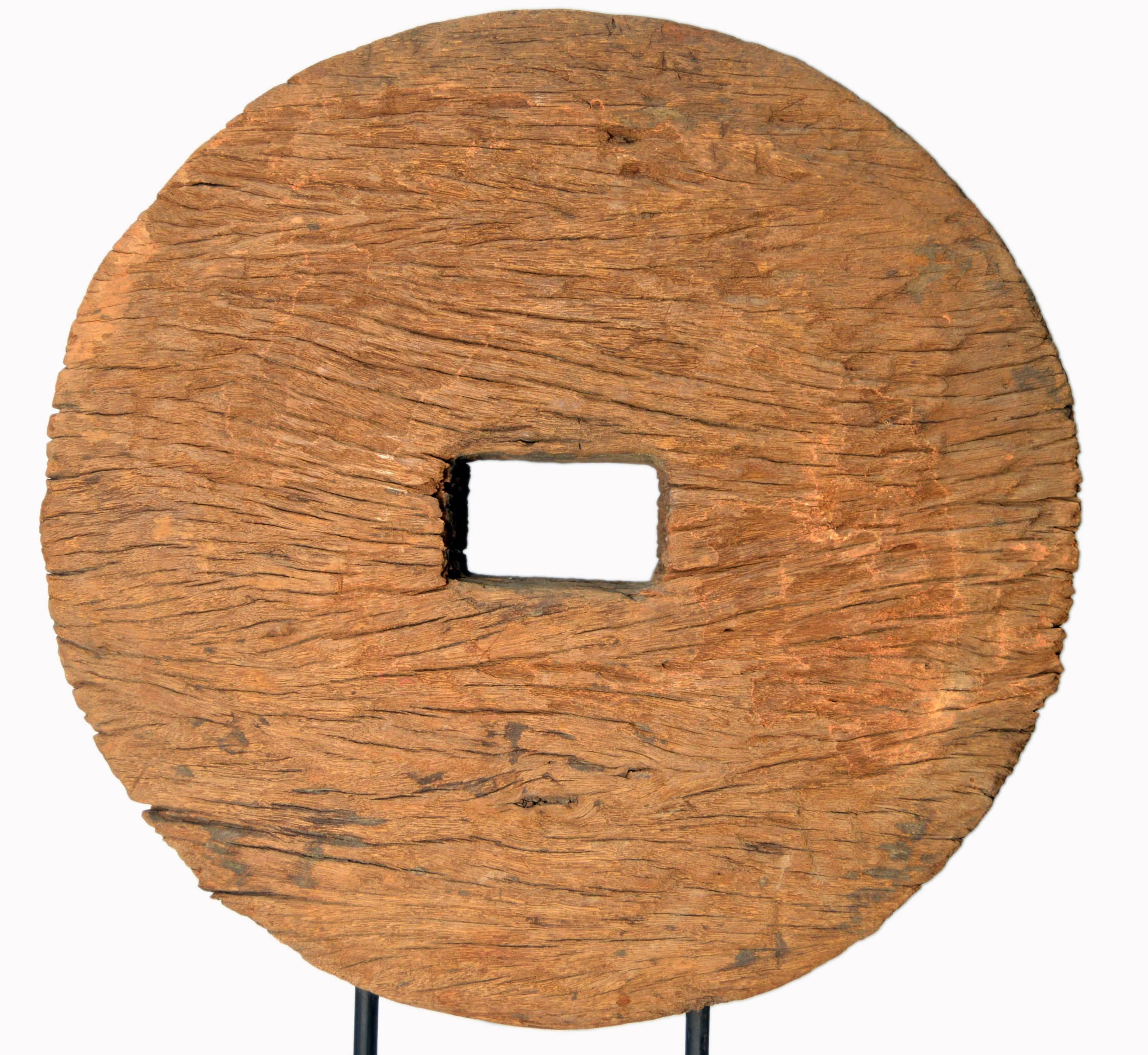 A Chinese 19th century rustic ox cart wooden wheel mounted on a custom made black stand. This handmade Chinese wheel is pierced in its center with a rectangular hole reserved for the axle tree. The wheel showcases a great weathered patina witnessing