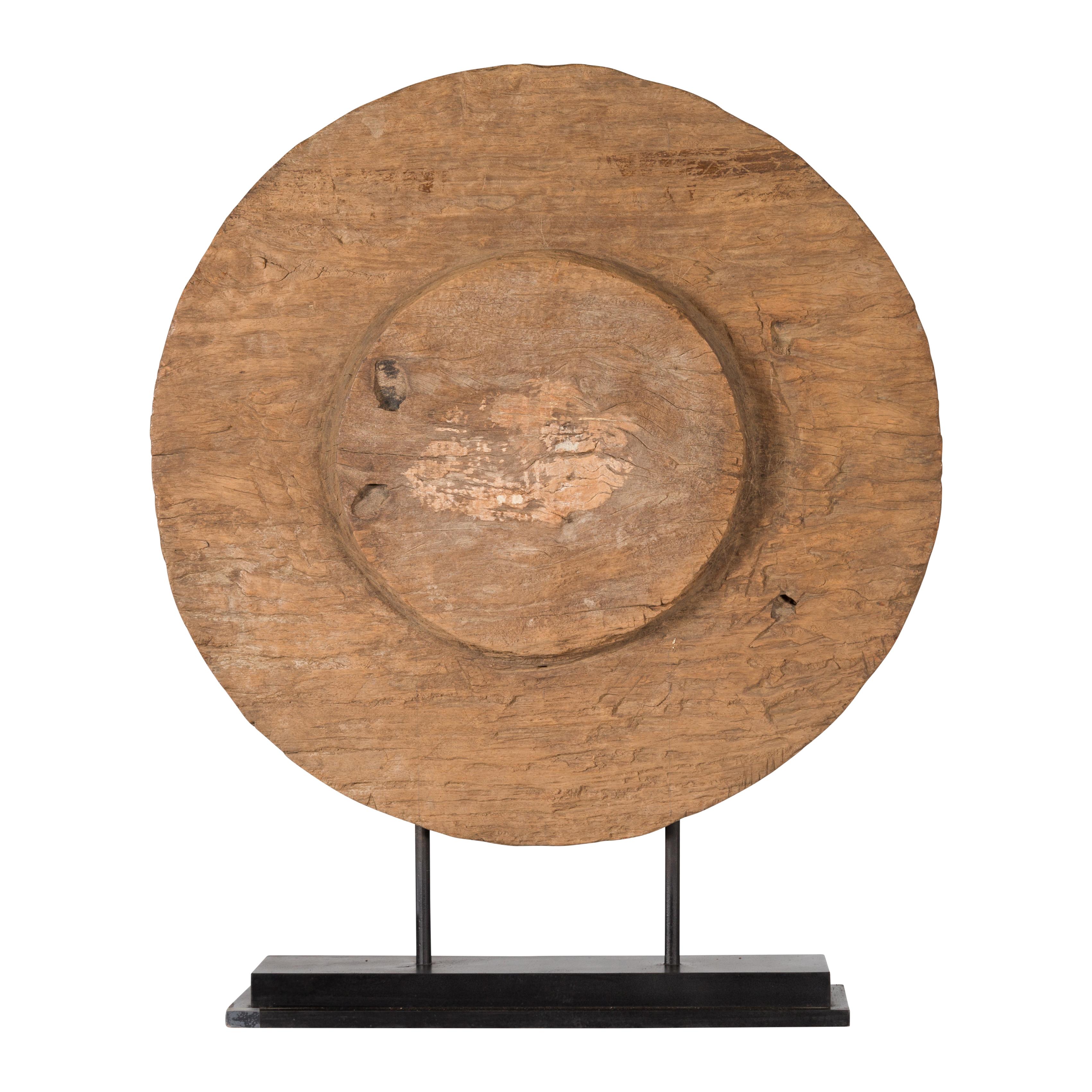 A Chinese 19th century rustic ox cart wooden wheel mounted on a custom made black stand. Created in China during the 19th century, this handmade wheel showcases a nicely weathered patina witnessing its long use since the Qing Dynasty. Mounted on a