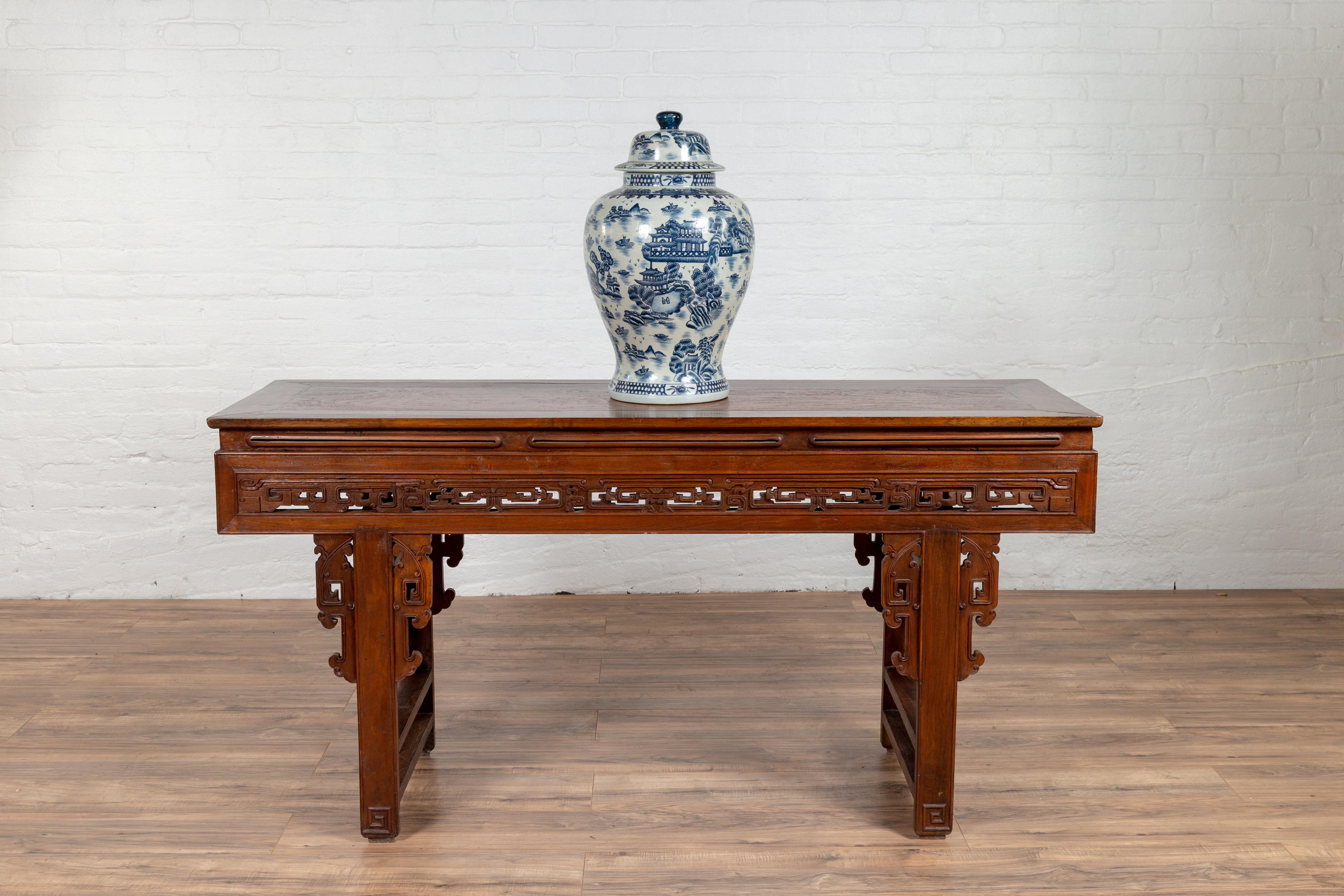 A Chinese antique altar console table with overhang top and open fretwork on scroll frieze from the early 20th century. This Chinese altar table charms our eyes with its exquisite Silhouette and delicate décor! It features a rectangular planked top