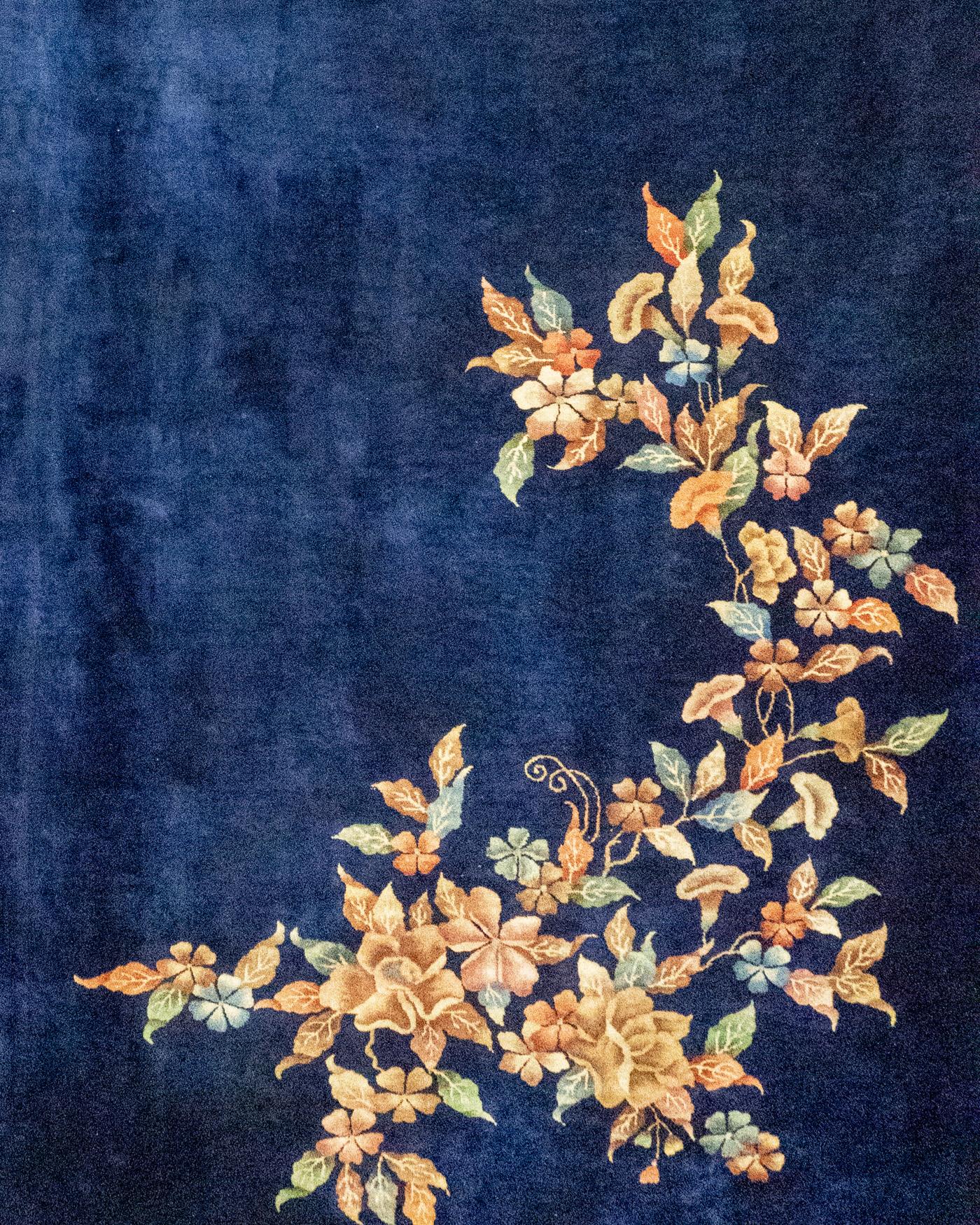 Antique Chinese Art Deco area rug 12' X 19'3. A wonderful example of a Chinese Art Deco style rug woven circa 1920 with a plain navy ground and in two opposing corners a delightful selection of flowers in a variety of soft and gentle colors. The Art