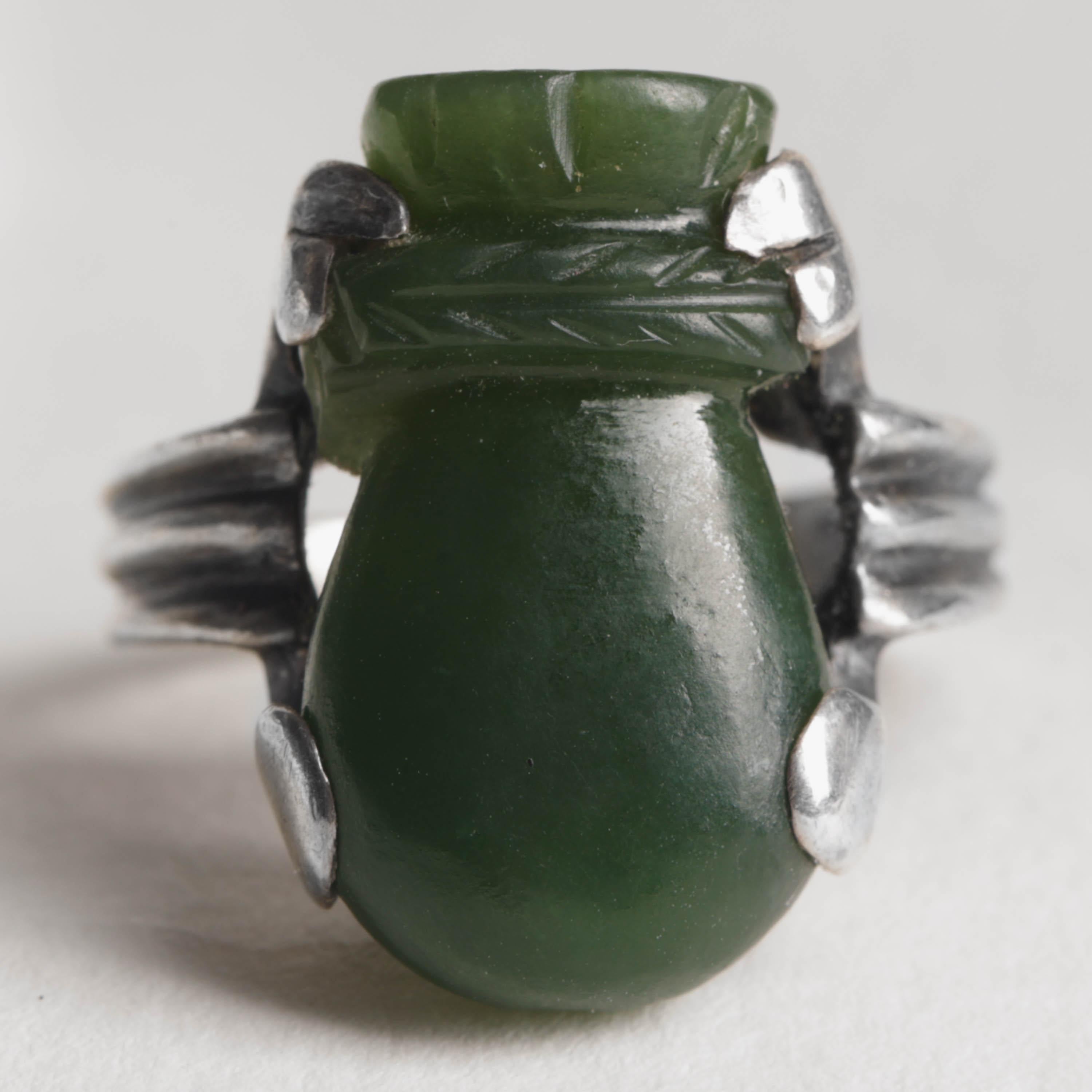 This Art Deco era ring (circa 1930s) features a hand-carved nephrite jade in the shape of a bottle gourd;  a powerful symbol in the historical Chinese culture endowed with magical significance. The bottle gourd carried medicine, water, and food; it