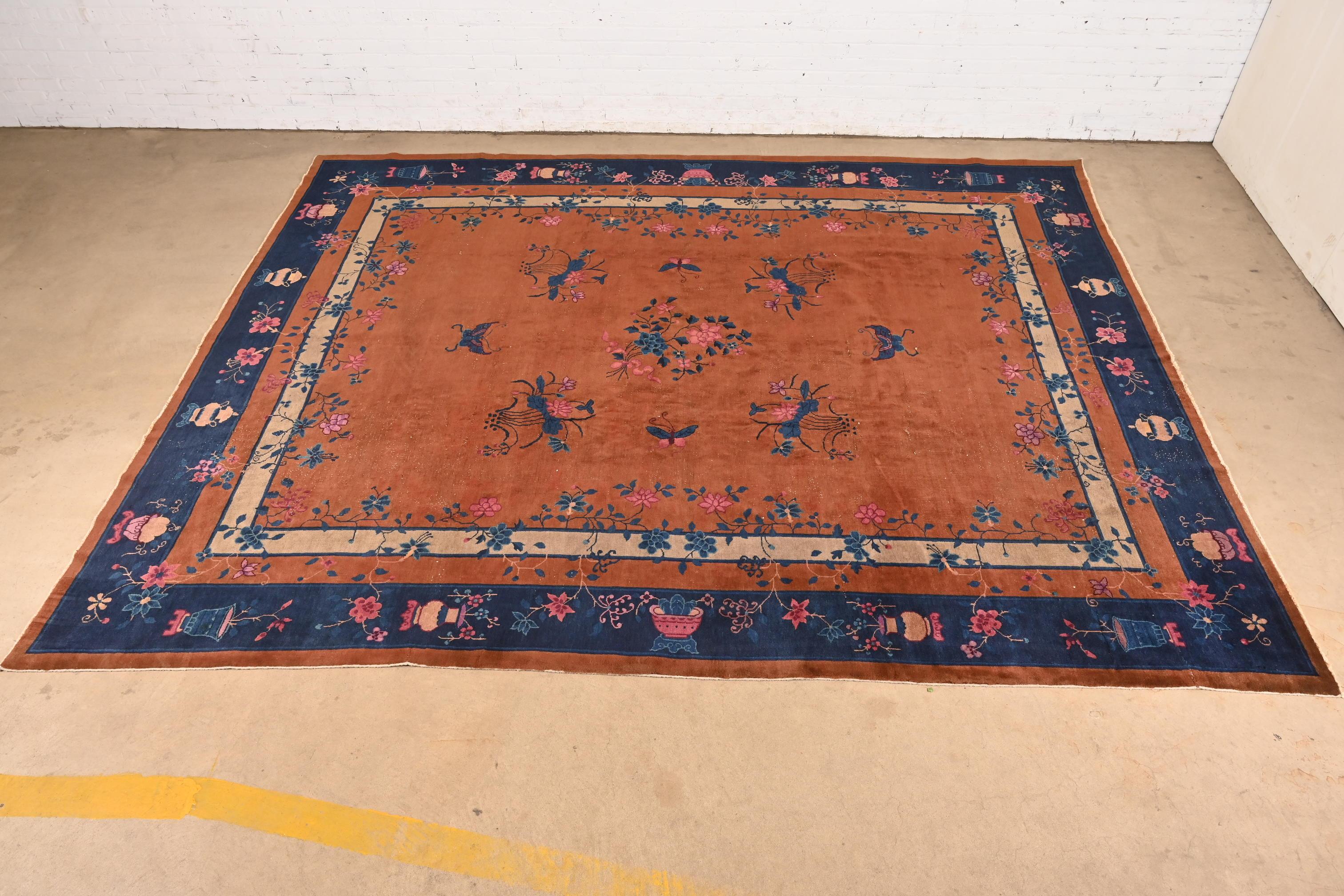Preciosa alfombra antigua de lana Nichols Art Decó china, anudada a mano, de tamaño grande para habitaciones

China, hacia 1920

Campo marrón, con borde azul y bonito diseño floral multicolor con urnas.

Medidas: 115