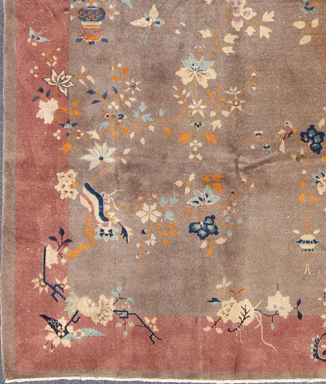 Handwoven in the first part of 20th Century, this antique Chinese rug features a light brown field with a rose and salmon border that decorates the uniquely colored piece. Inspired by ancient Chinese motifs, the Art Deco design reflects the