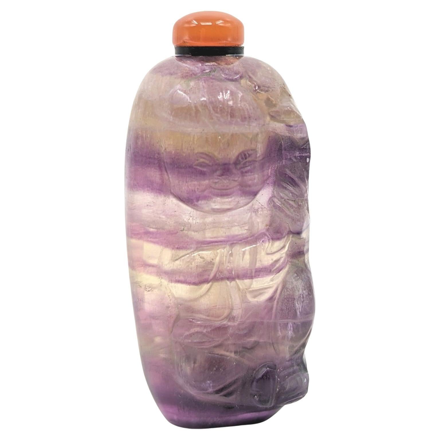 An antique banded amethyst quartz snuff bottle, well carved in the figure of a child holding a lotus leaf. The beautiful quartz material displays vibrant purple bands of amethyst, on a flat foot ring, with an orange agate stopper

Height: