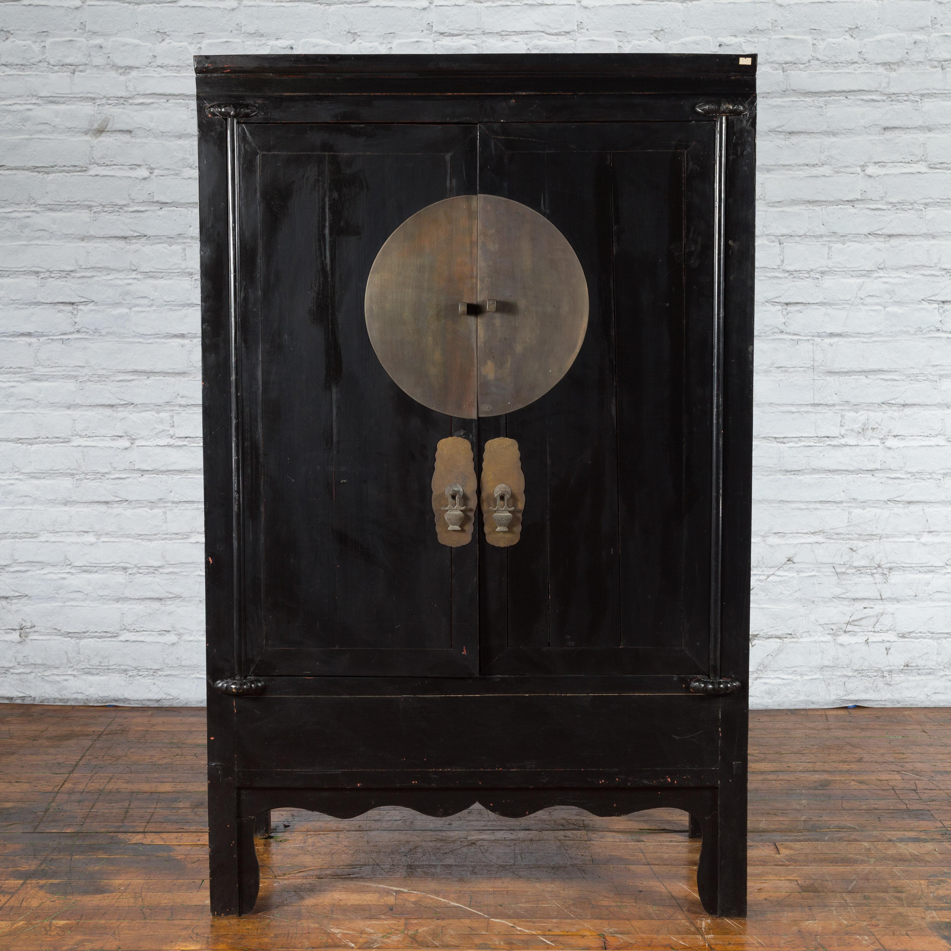 An antique Chinese wedding cabinet from the early 20th century with black lacquer and large brass medallion hardware. Created in China during the early years of the 20th century, this wedding cabinet features a black lacquered ground perfectly